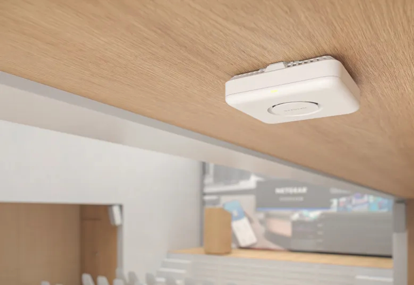Biały punkt dostępowy zamontowany na drewnianym suficie. Tło przedstawia rozmyty pokój z brązowym przedmiotem.