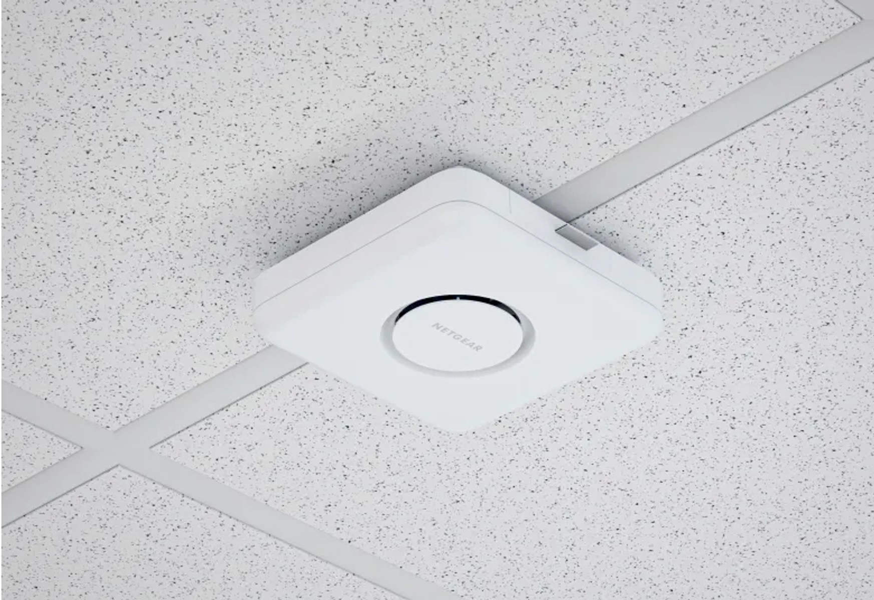 Biały punkt dostępowy Netgear zamontowany na nakrapianym suficie. Urządzenie jest kwadratowe z okrągłym środkiem.