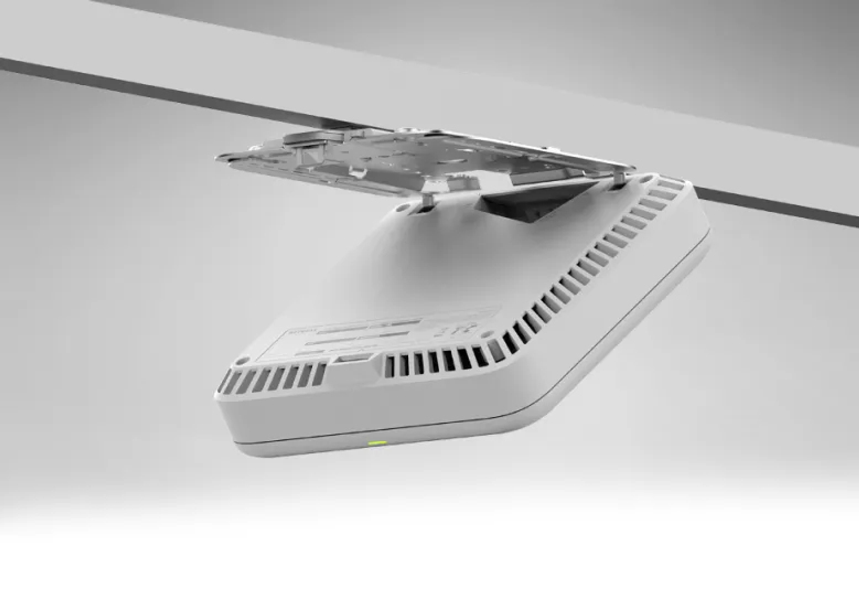 Białe urządzenie zamontowane na suficie. Ma prostokątny kształt z otworami wentylacyjnymi i zielonym światłem. Jego górna część jest otwarta.