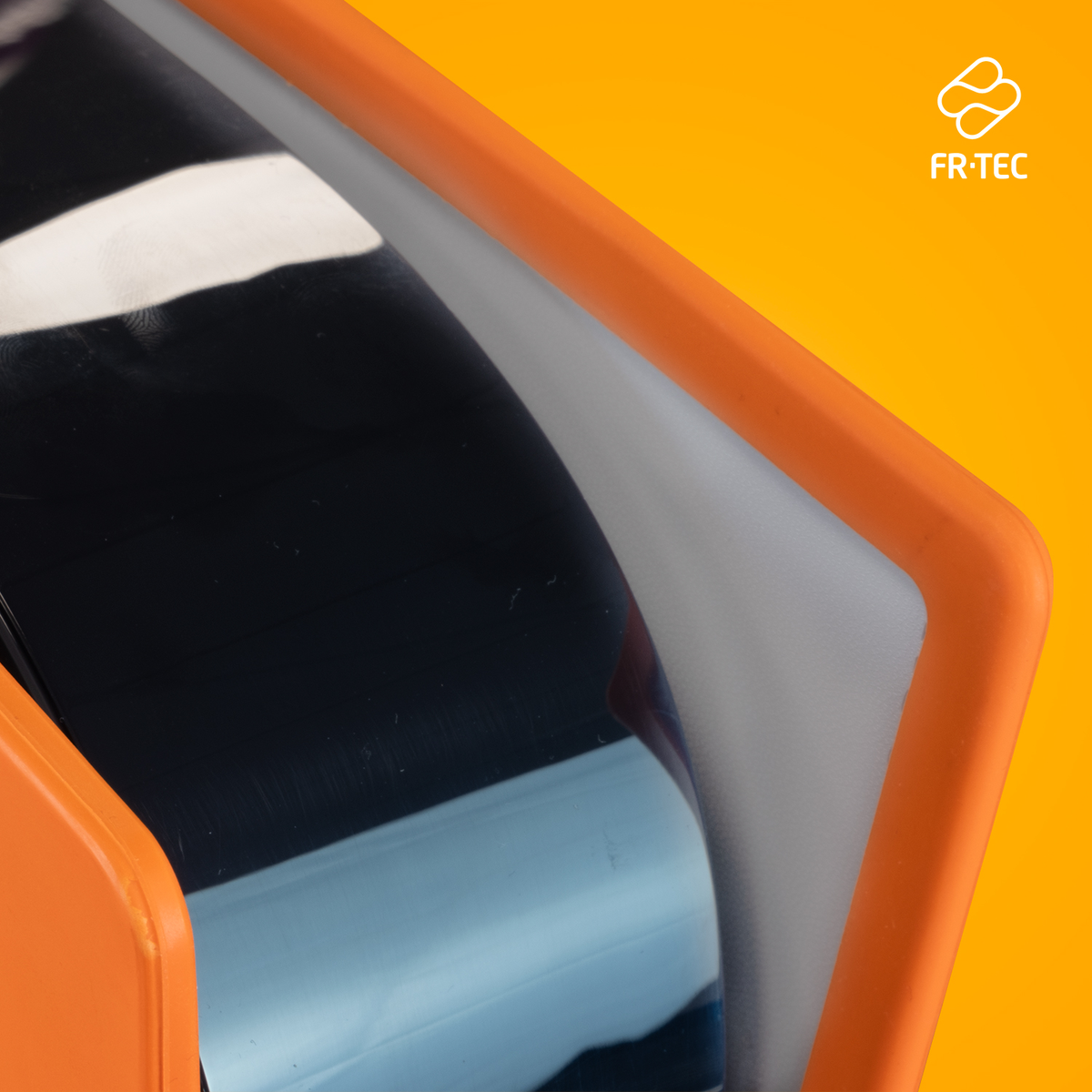 Primer plano de una superficie negra reflectante dentro de un marco naranja, sobre un fondo amarillo con un logo.