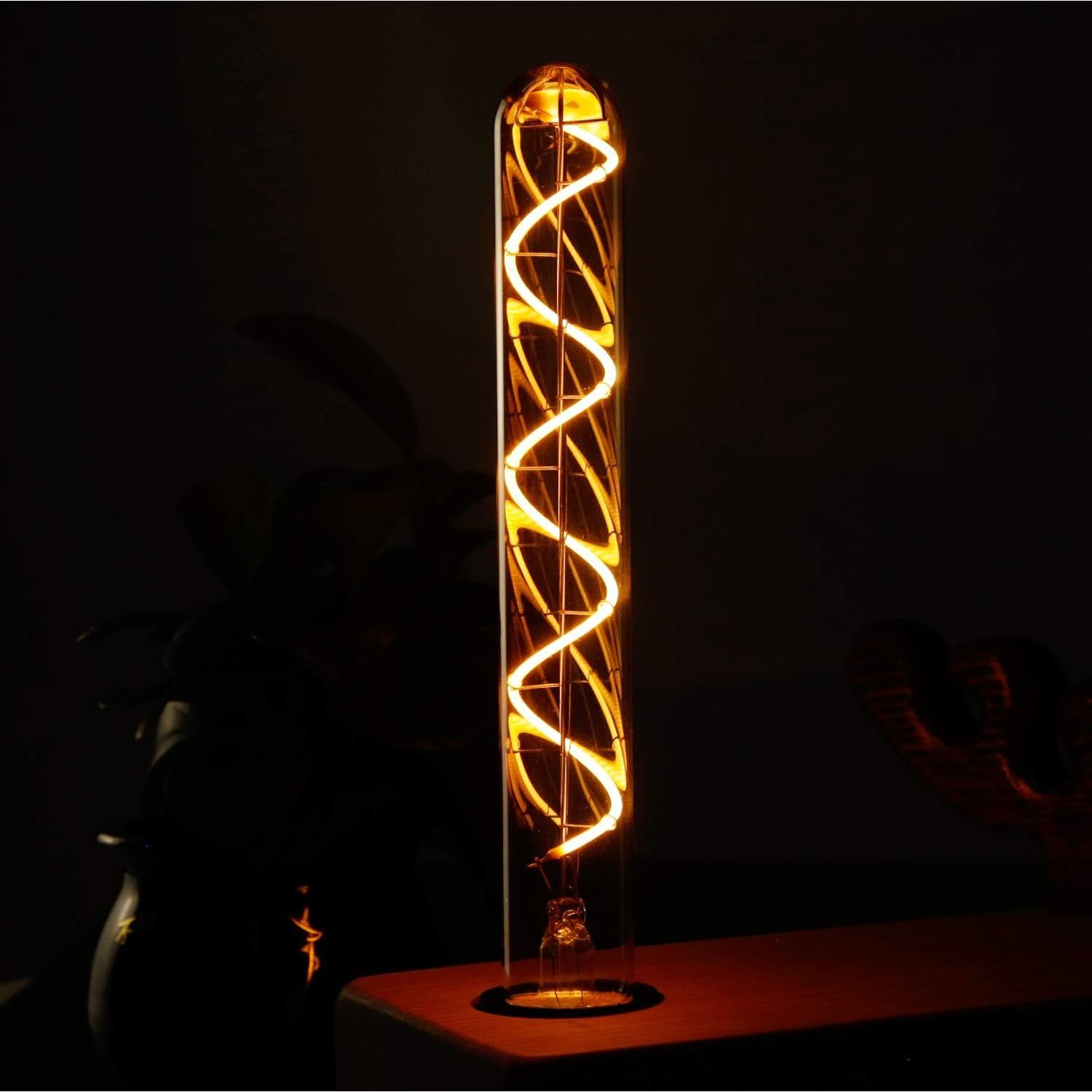 Długa, podświetlona żarówka z spiralnym włóknem. Żarówka stoi na drewnianej powierzchni na ciemnym tle.