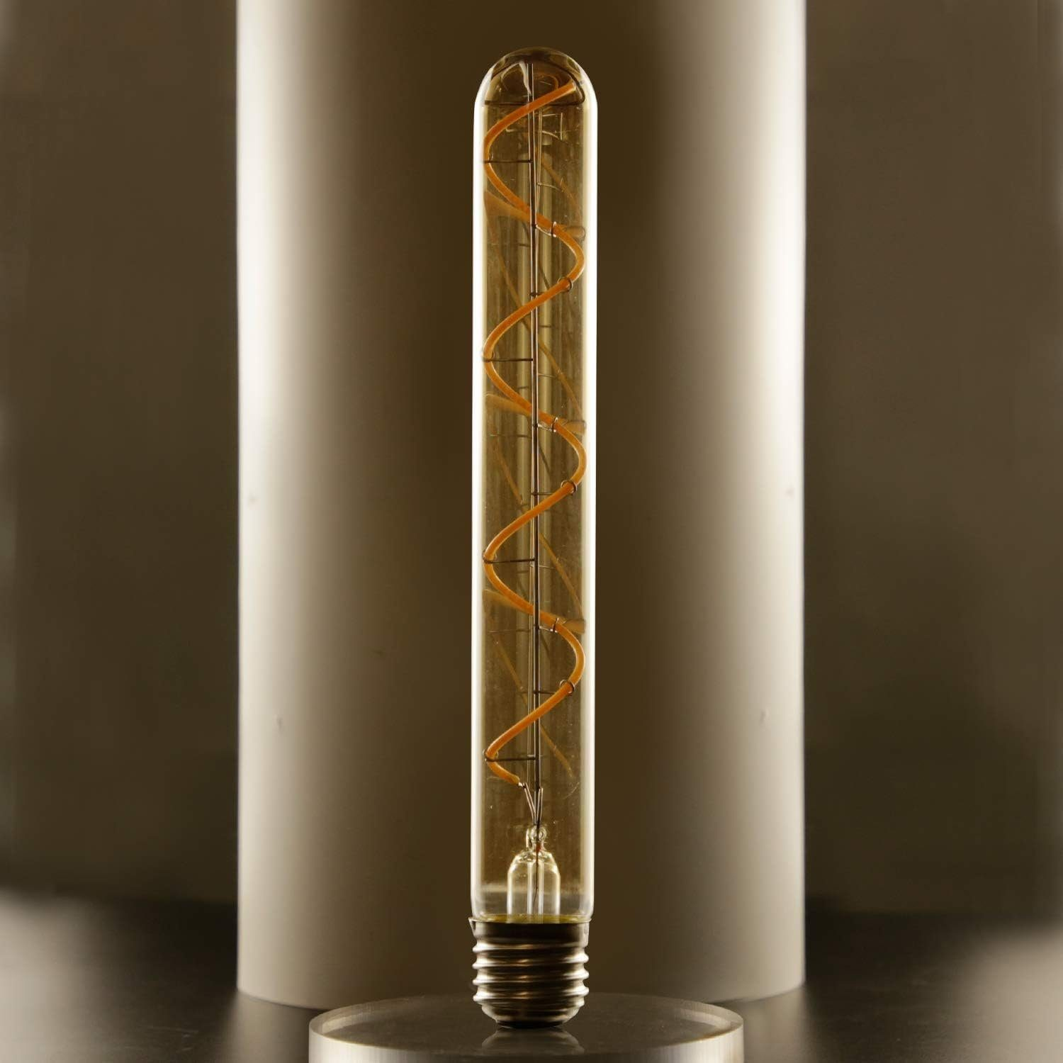 Żarówka rurowa ze spiralnym żarnikiem, stojąca przed białym walcem na ciemnej powierzchni.