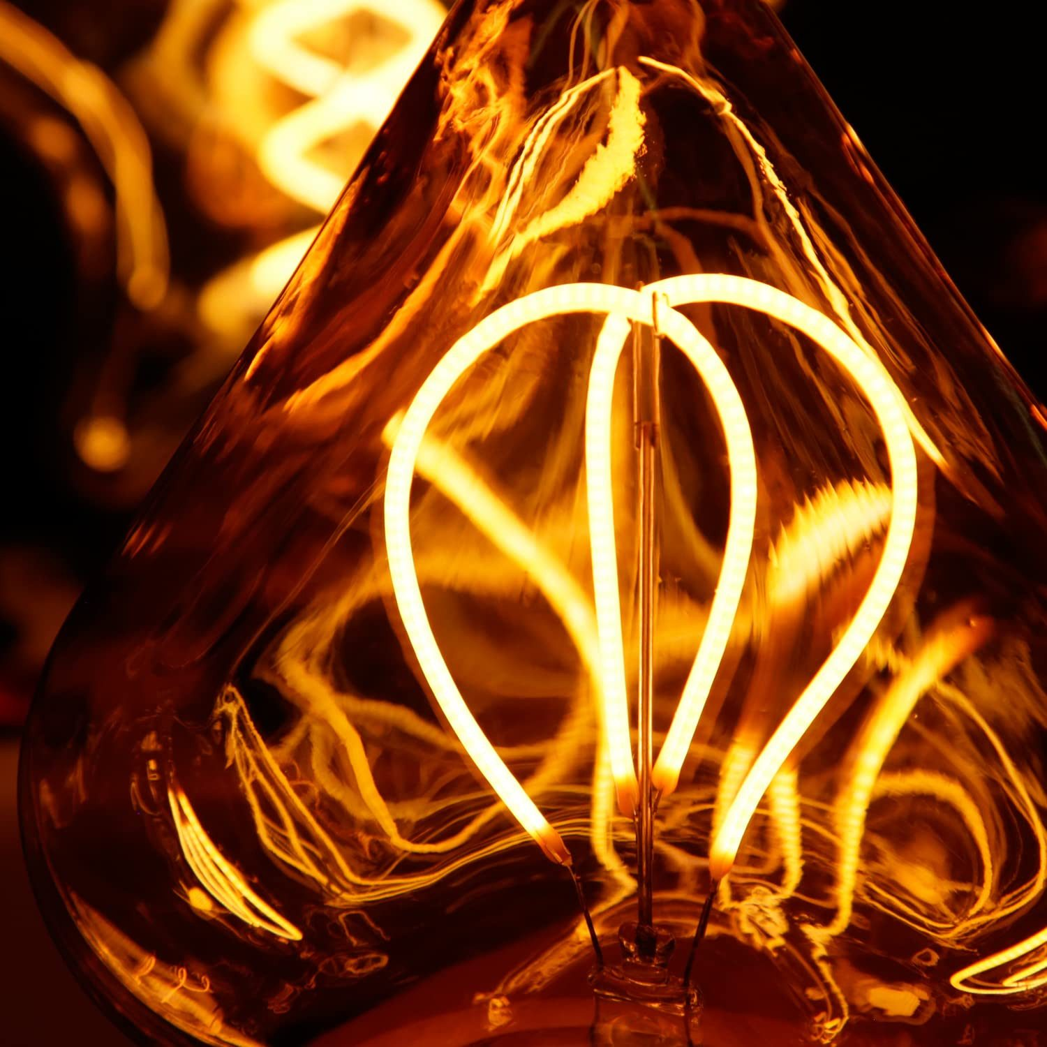 Zbliżenie żarzącej się żarówki. Włókno ma kształt serca. Ciepłe żółte światło na ciemnym tle.
