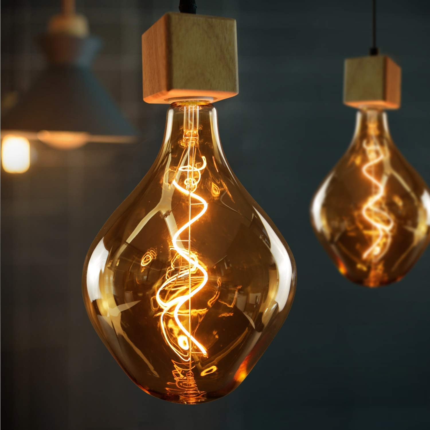 Due lampadine decorative con cime in legno sono appese su uno sfondo scuro. Le lampadine sono ambrate calde con filamento visibile.