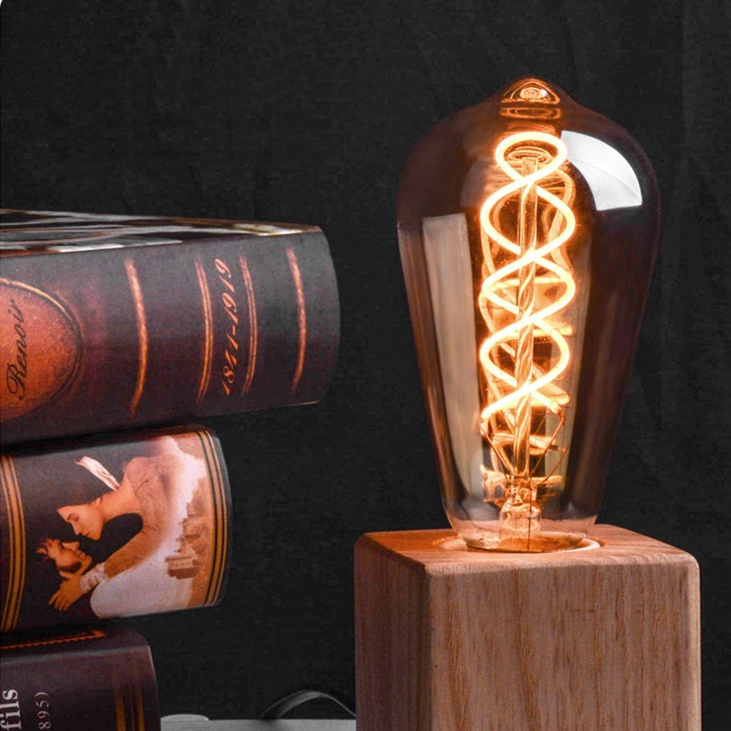 Żarówka Edisona na drewnianej podstawie obok ułożonych książek. Żarówka jest zapalona, z widocznym spiralnym włóknem.