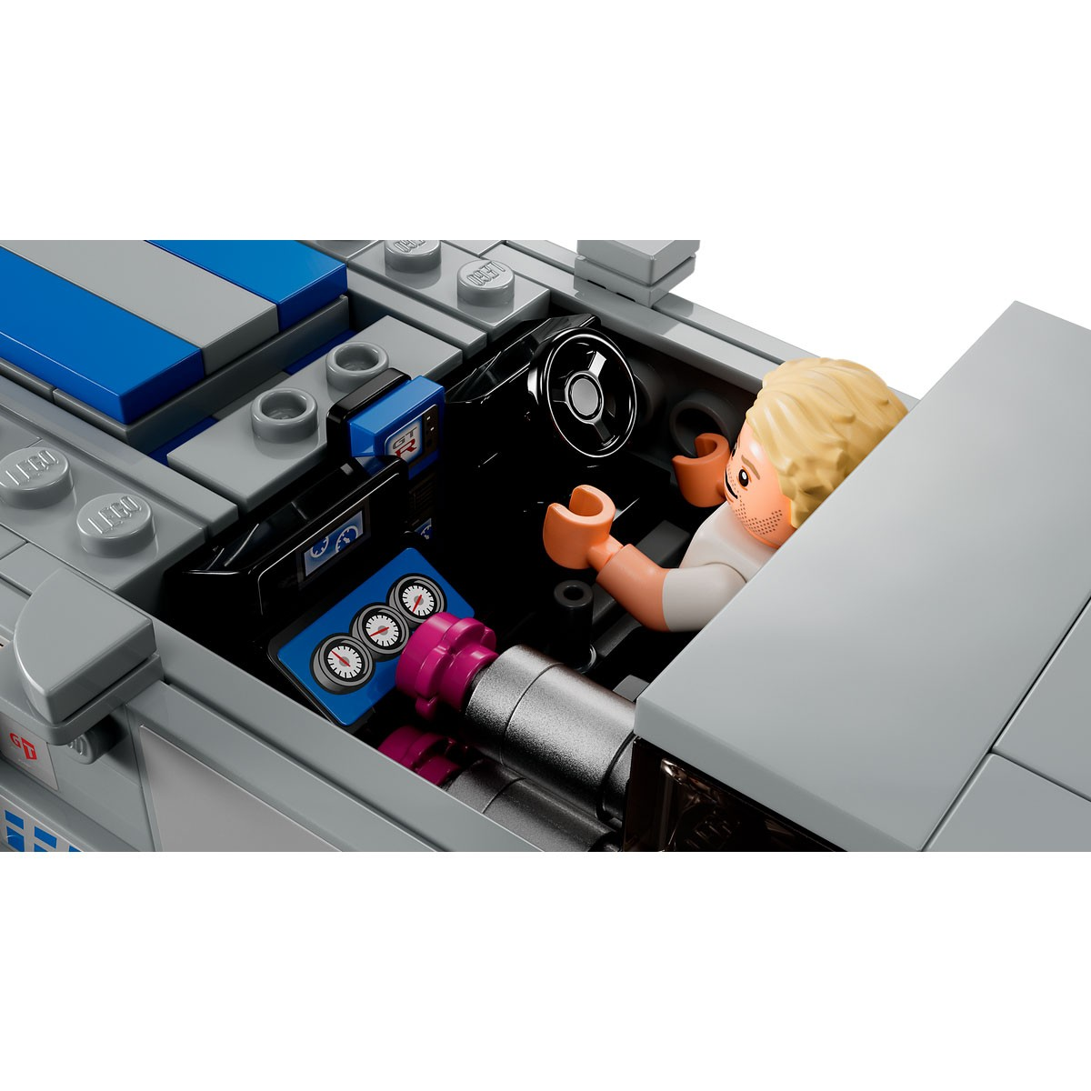 Interior de un coche Lego. Una figura Lego rubia está al volante. Los detalles del salpicadero incluyen diales e indicadores. El coche es gris.
