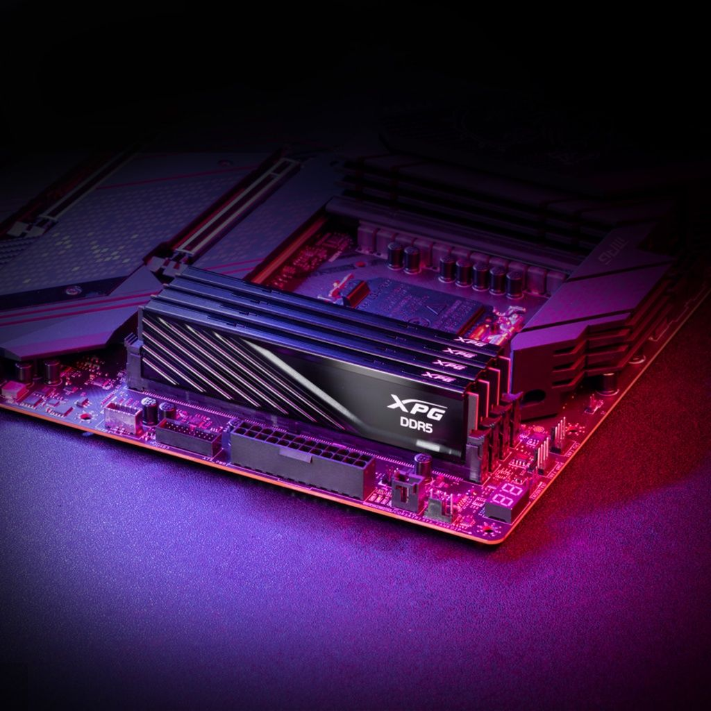 Płyta główna komputera z zainstalowanym czarnym modułem RAM XPG DDR5. Płyta jest oświetlona fioletowym i czerwonym światłem.