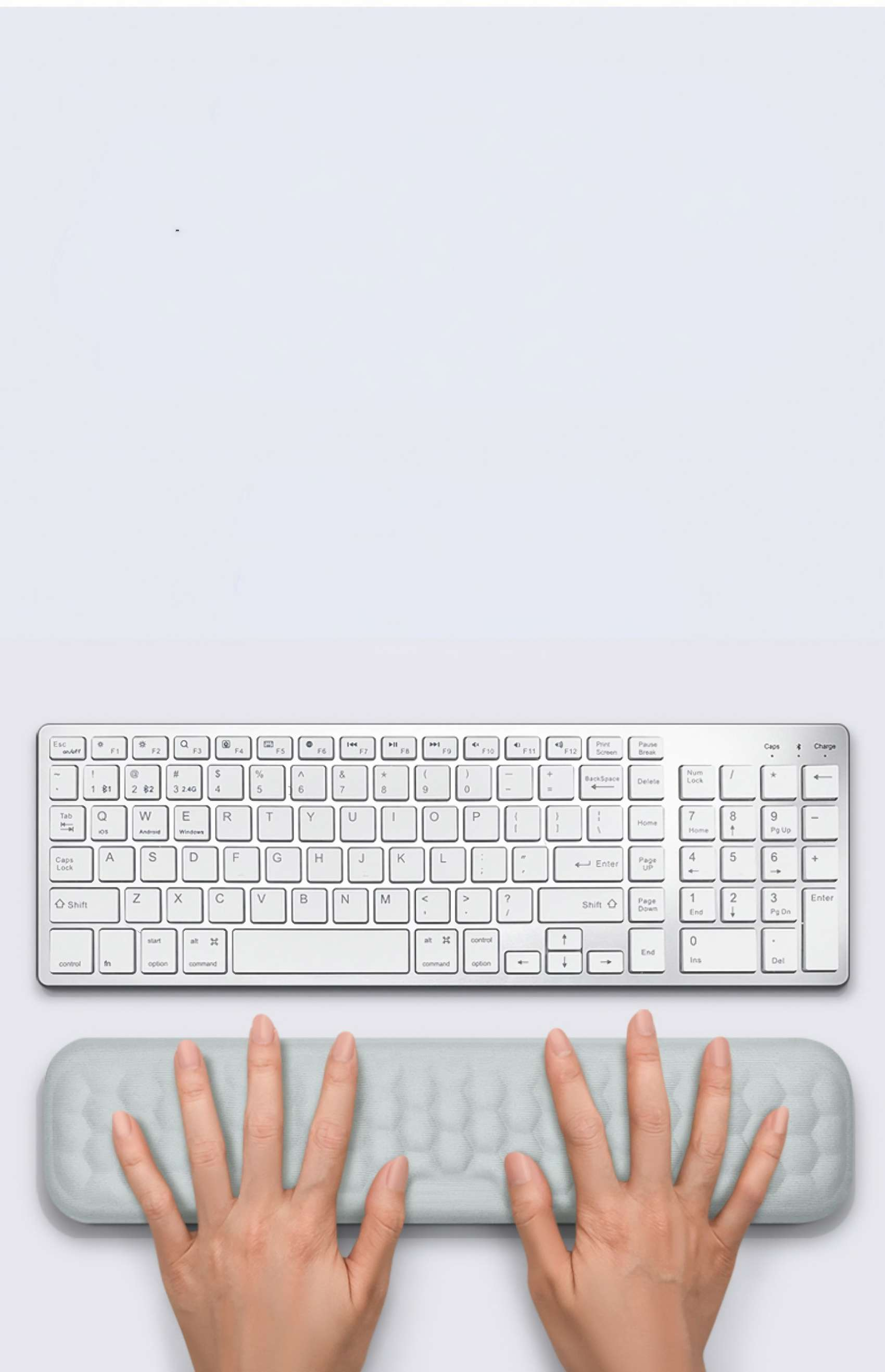 Eine weiße Tastatur mit Handballenauflage und zwei Händen darauf. Der Hintergrund ist weiß.