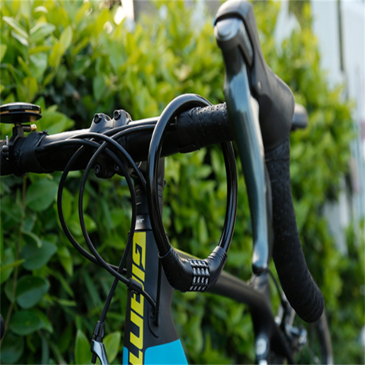 Zbliżenie kierownicy roweru z czarną blokadą. Zielone liście w tle. Kierownice są czarne z czarną i niebieską ramą roweru.