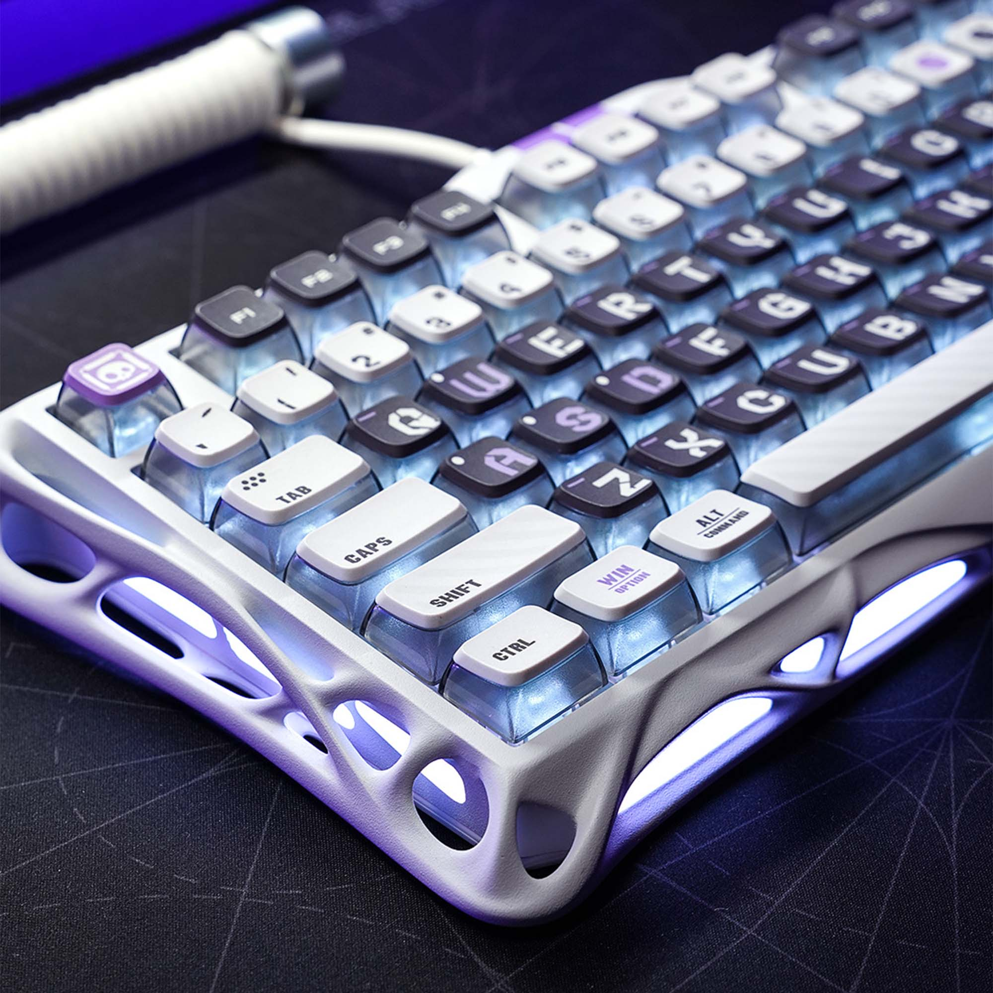 Zbliżenie białej i fioletowej klawiatury mechanicznej z podświetlanymi klawiszami. Klawisze mają przezroczyste nakładki. Klawiatura znajduje się na czarnej powierzchni.
