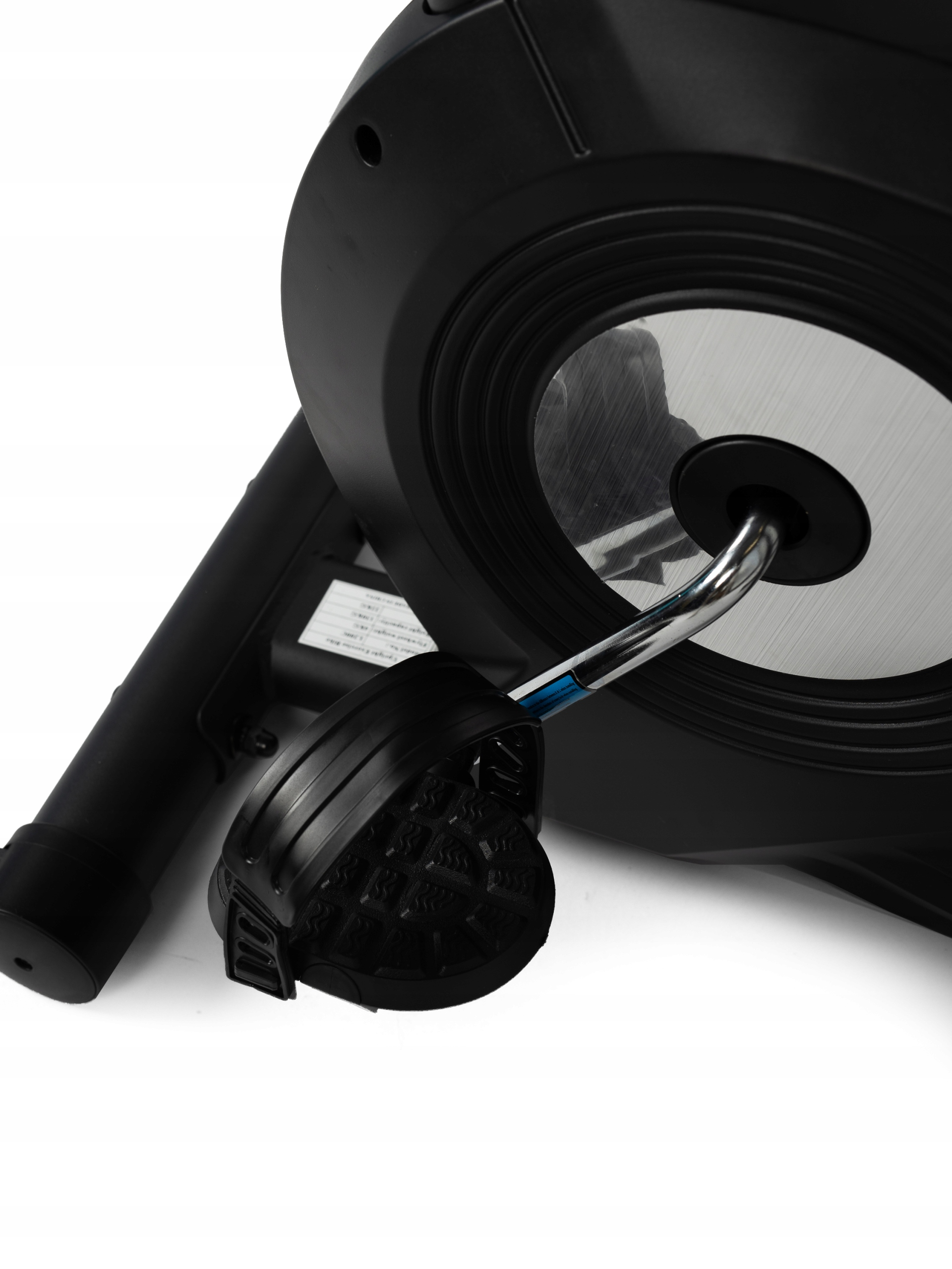 Zbliżenie czarnego pedału roweru treningowego, błyszczącego metalowego drążka i koła zamachowego na białym tle.