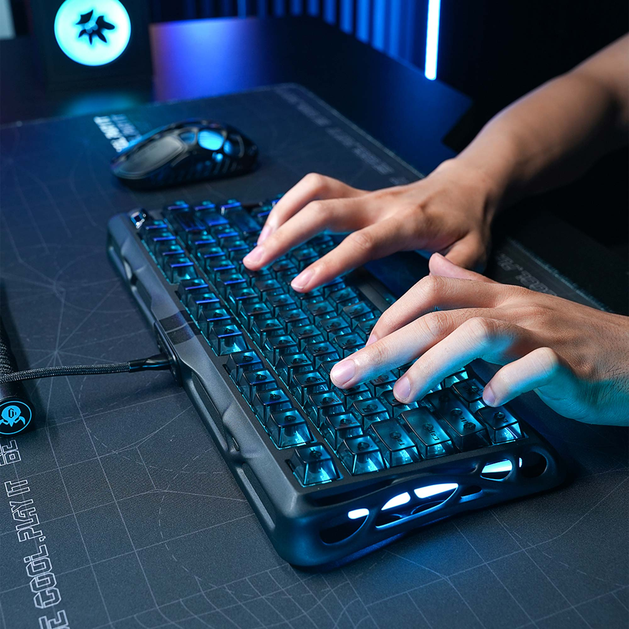 Ręce piszące na świecącej na niebiesko klawiaturze. Mysz i logo w tle. Scena jest ciemna i futurystyczna.