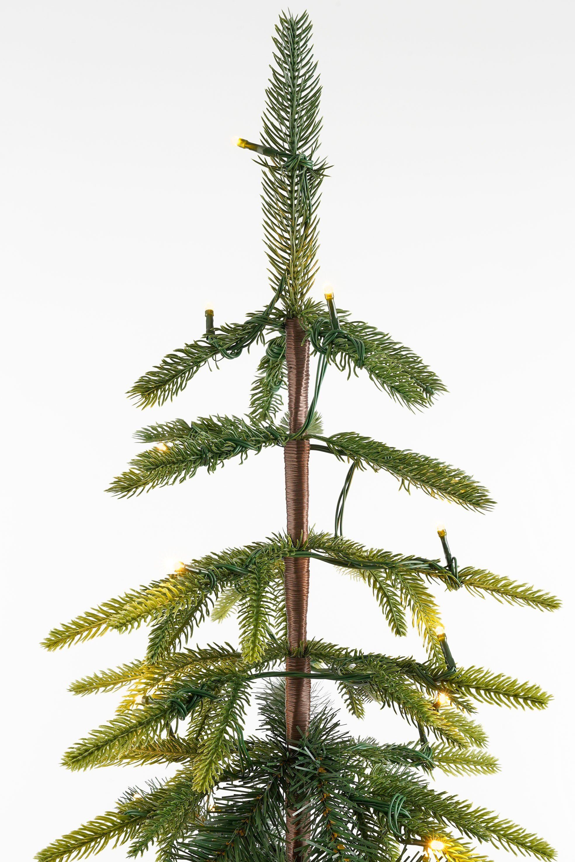 Un petit sapin de Noël artificiel est centré. Il a des aiguilles vertes, des lumières et un tronc brun, sur fond blanc.
