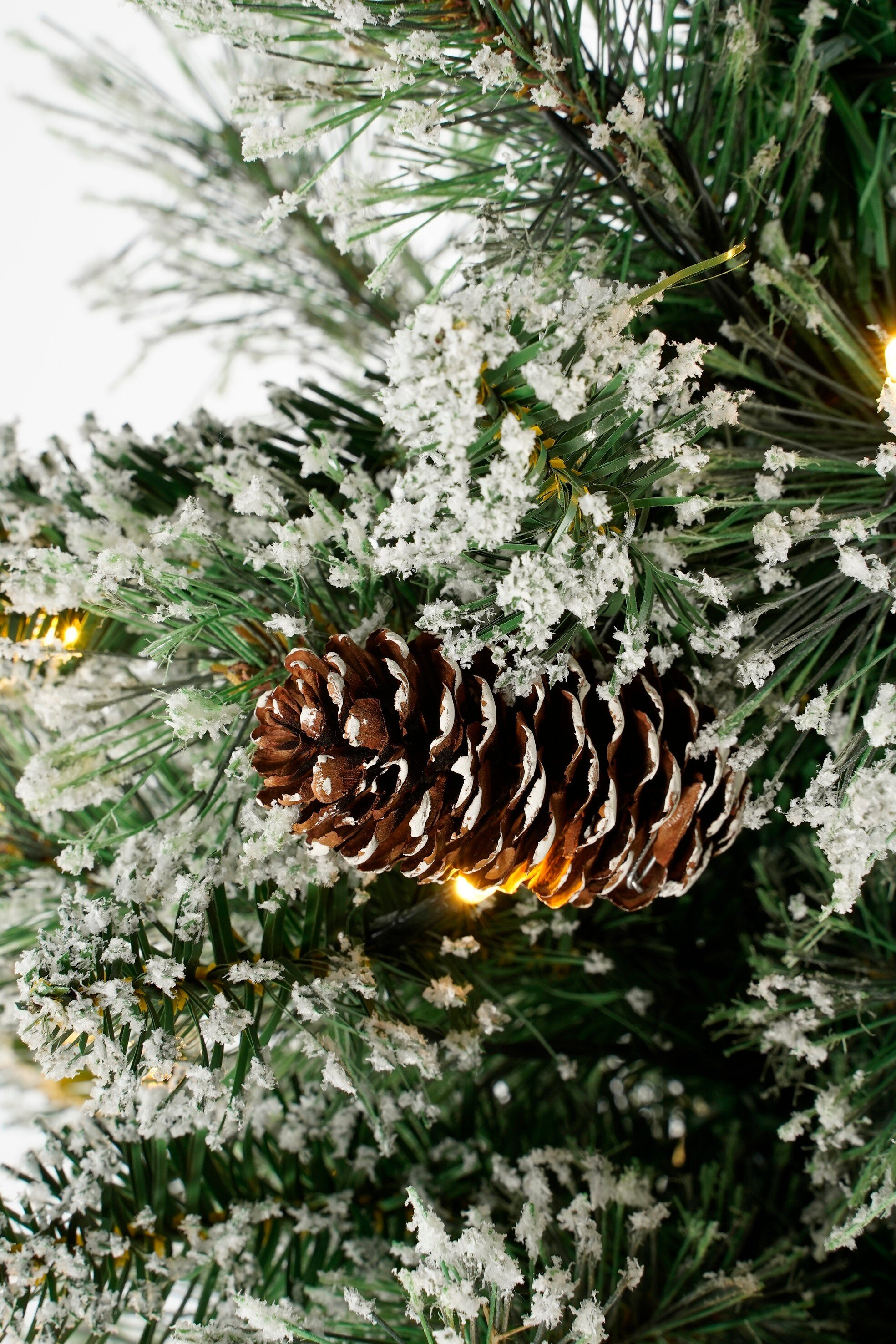 Gros plan sur un sapin de Noël décoré. Un grand cône de pin est au milieu d'aiguilles vertes recouvertes de neige artificielle.