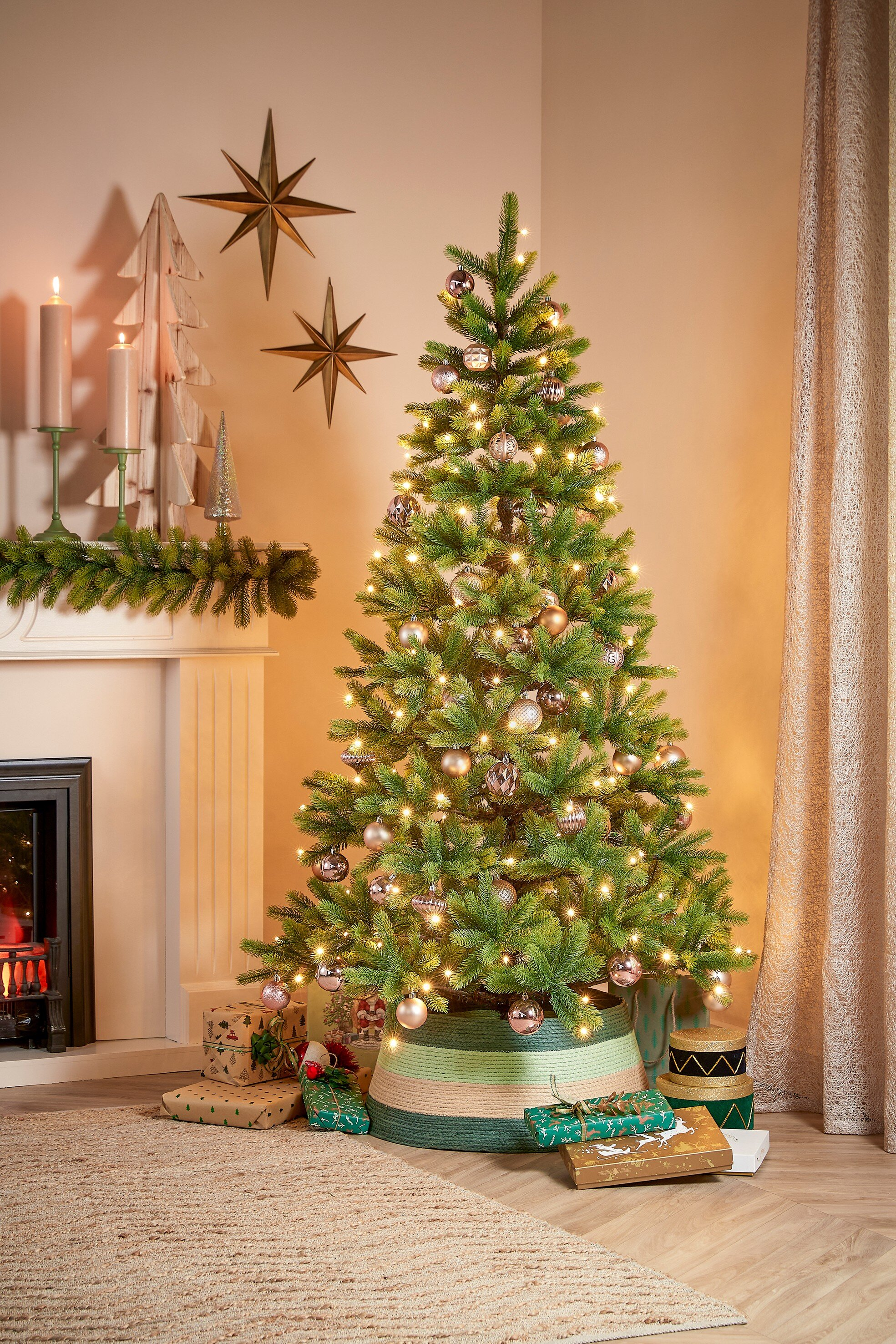 Sapin de Noël avec ornements et lumières, cadeaux, cheminée, bougies et décorations en étoile. Scène chaleureuse et festive.