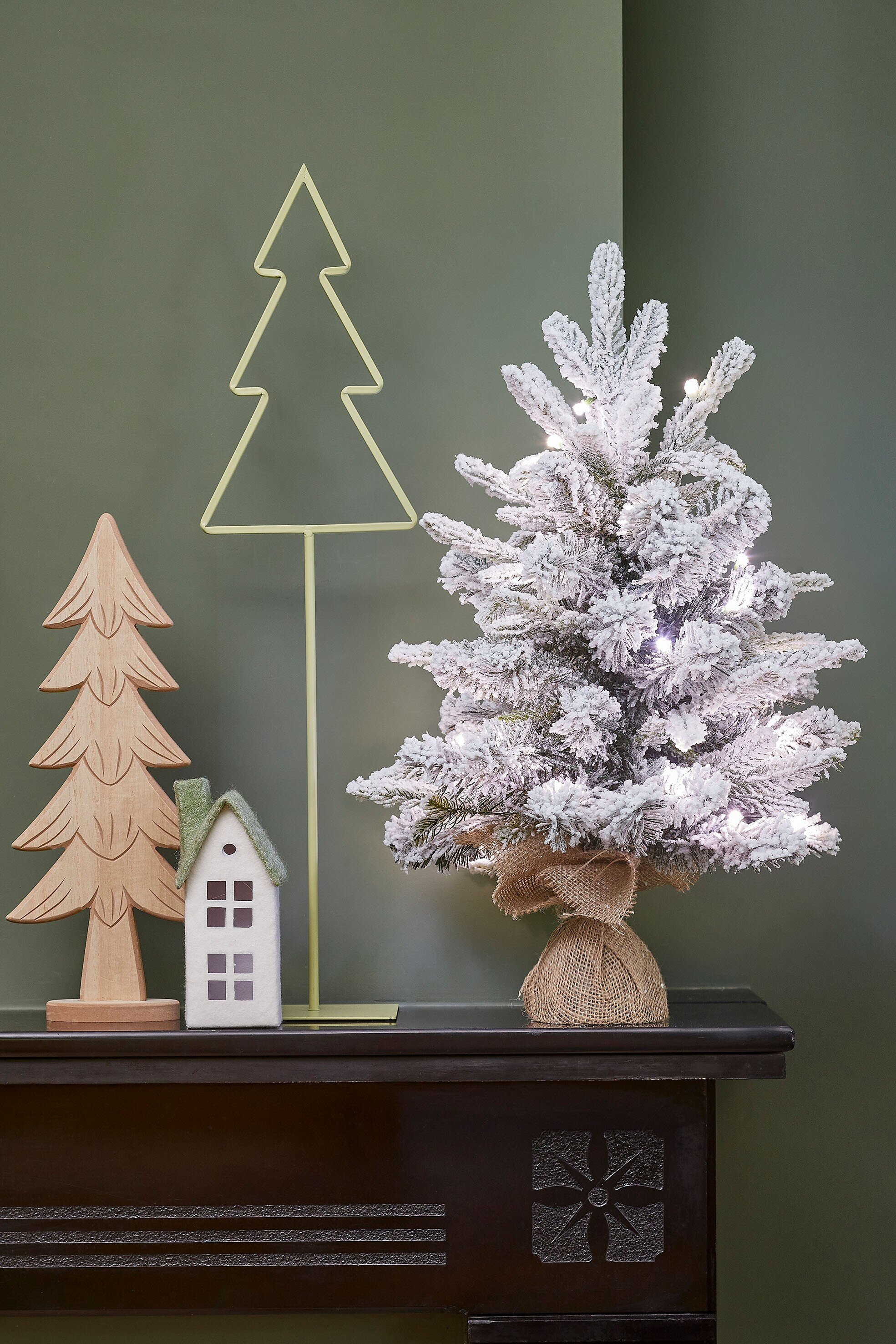 Une scène de Noël avec trois arbres, une maison, sur une surface sombre et un mur vert.