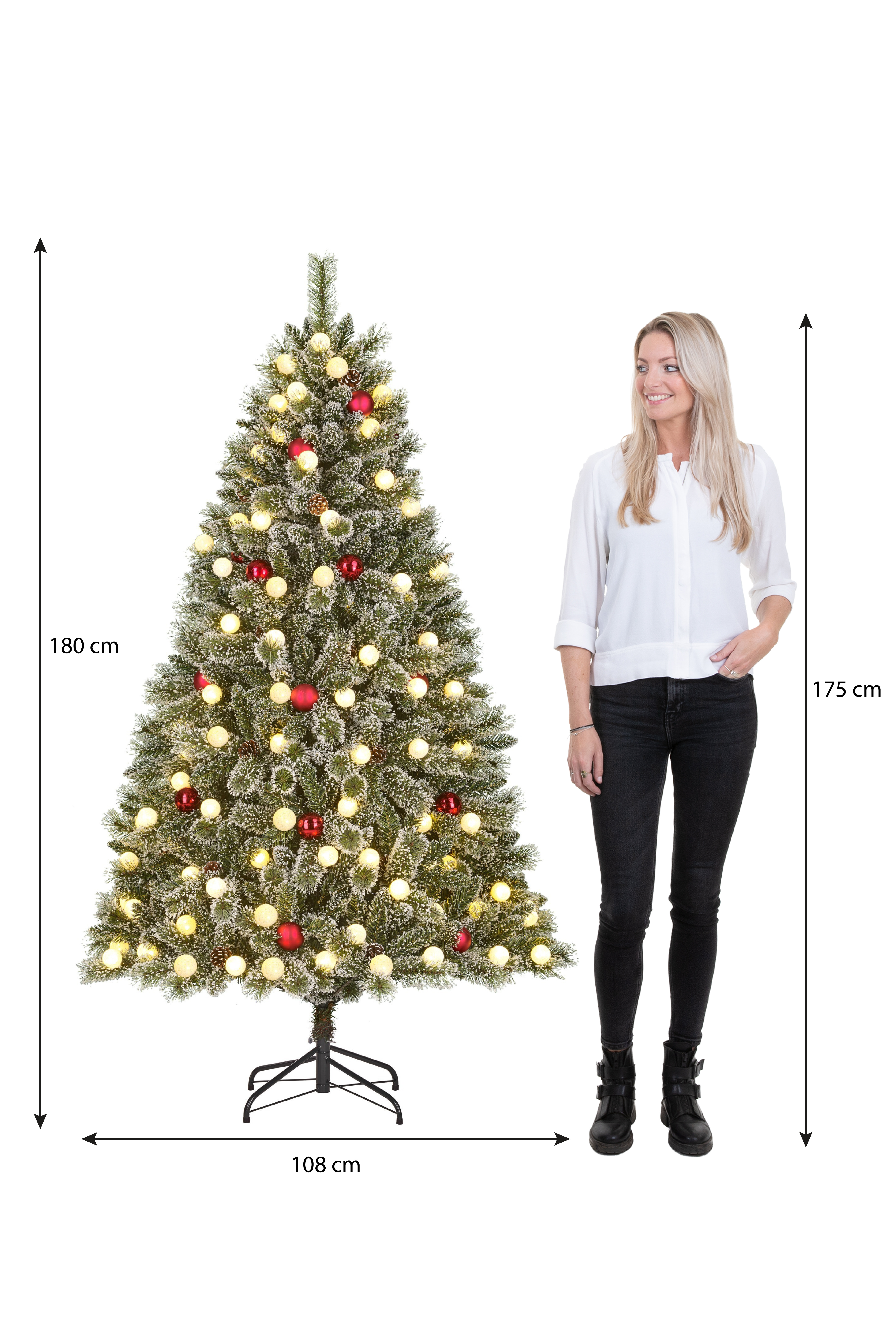 Une femme se tient près d'un sapin de Noël décoré. L'arbre est illuminé avec des lumières et des ornements. Des mesures sont affichées.
