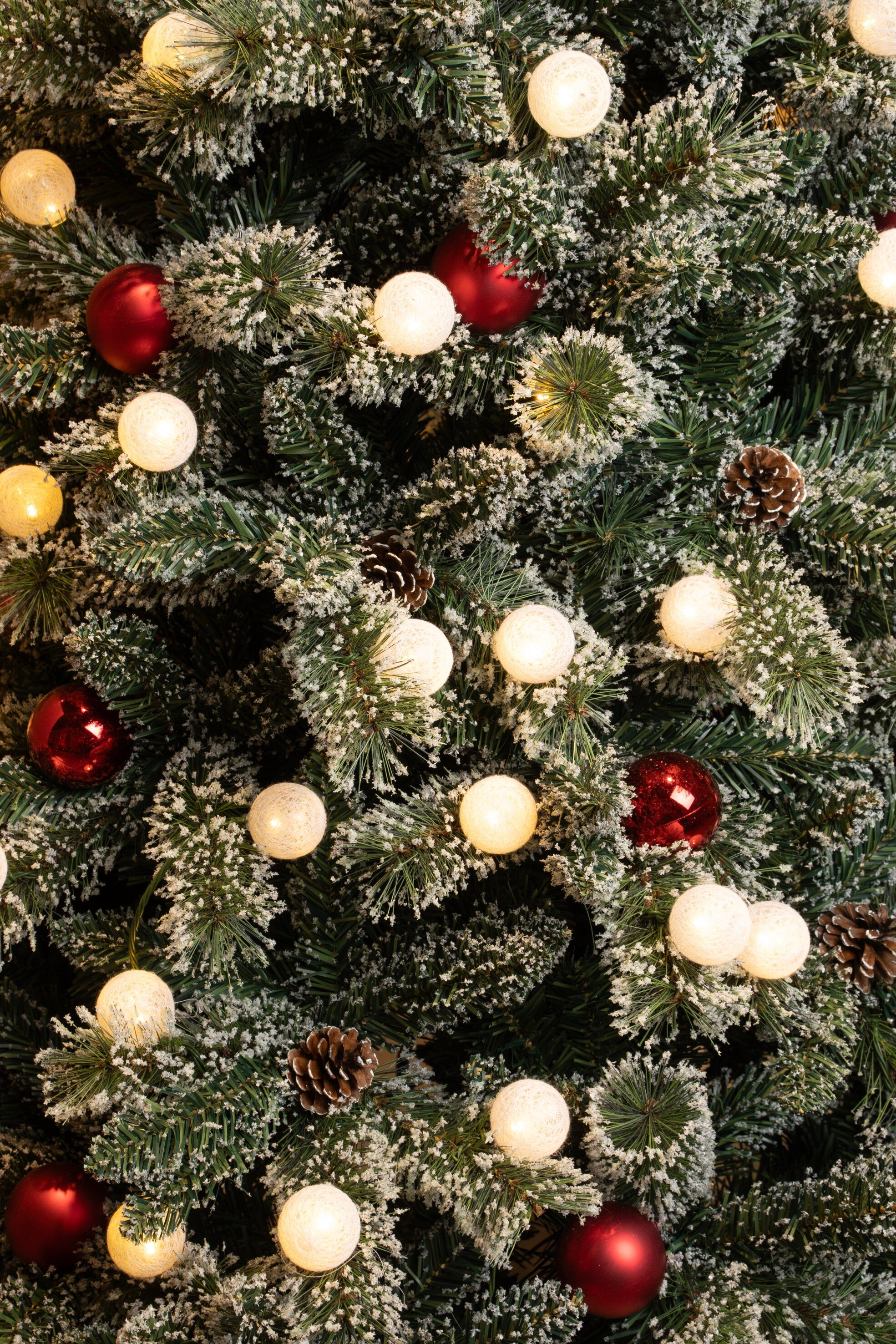 Un sapin de Noël avec des ornements rouges, des pommes de pin et des lumières blanches. Branches givrées.