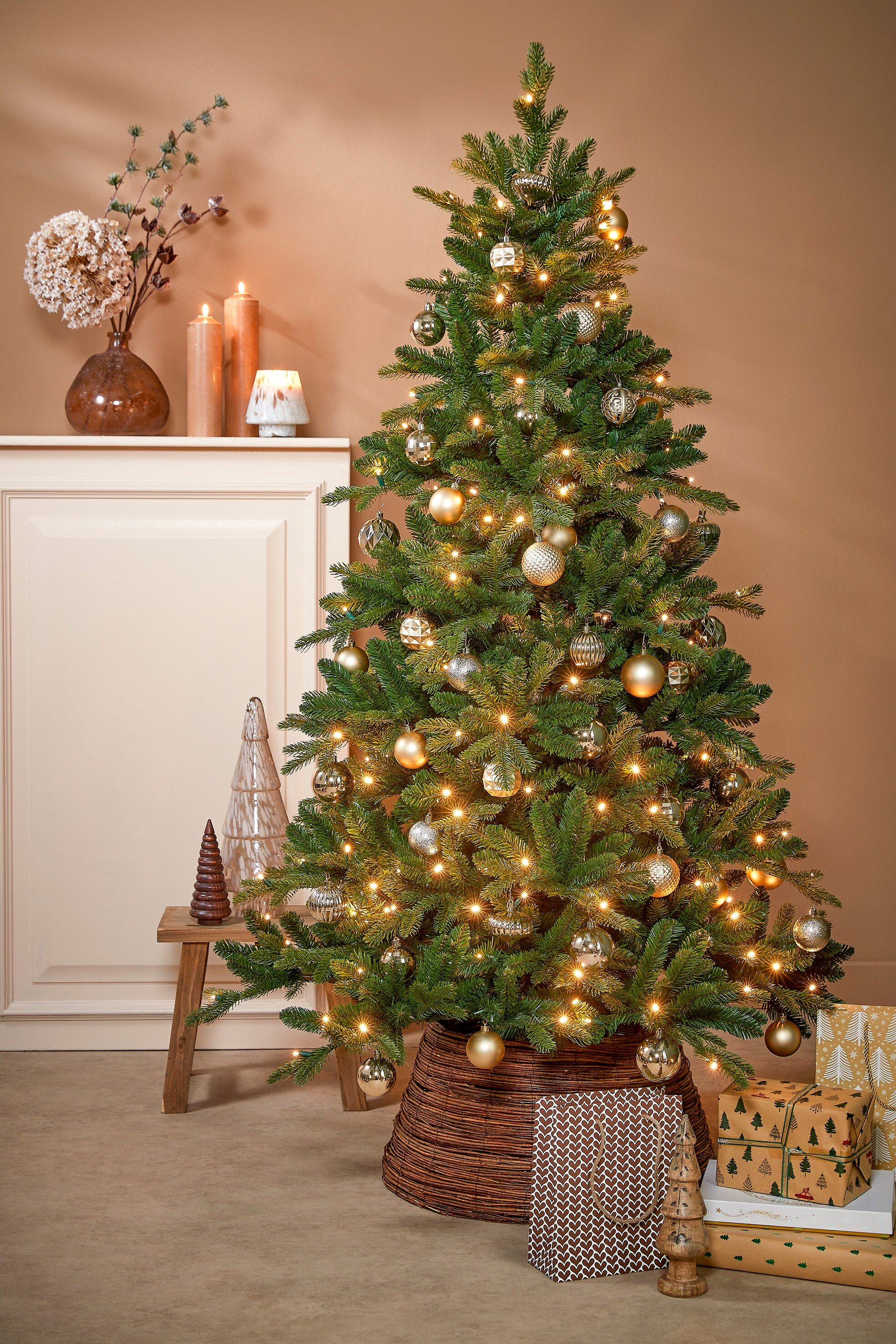 Sapin de Noël avec ornements et lumières, cadeaux en dessous. Bougies et décorations à gauche. Mur marron en arrière-plan.