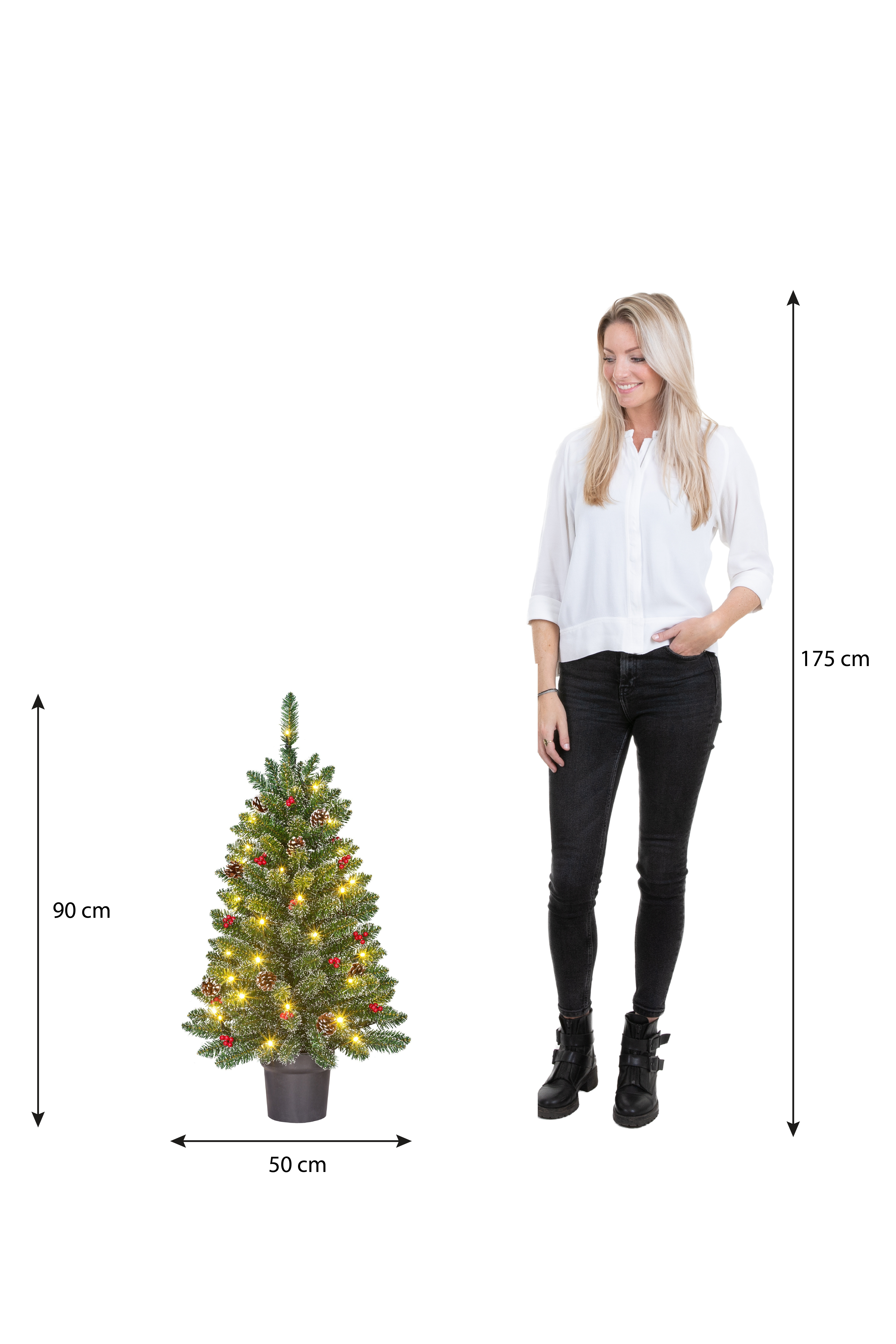 Une femme est à côté d'un sapin de Noël. L'arbre a des lumières et des ornements. Les mesures sont indiquées.