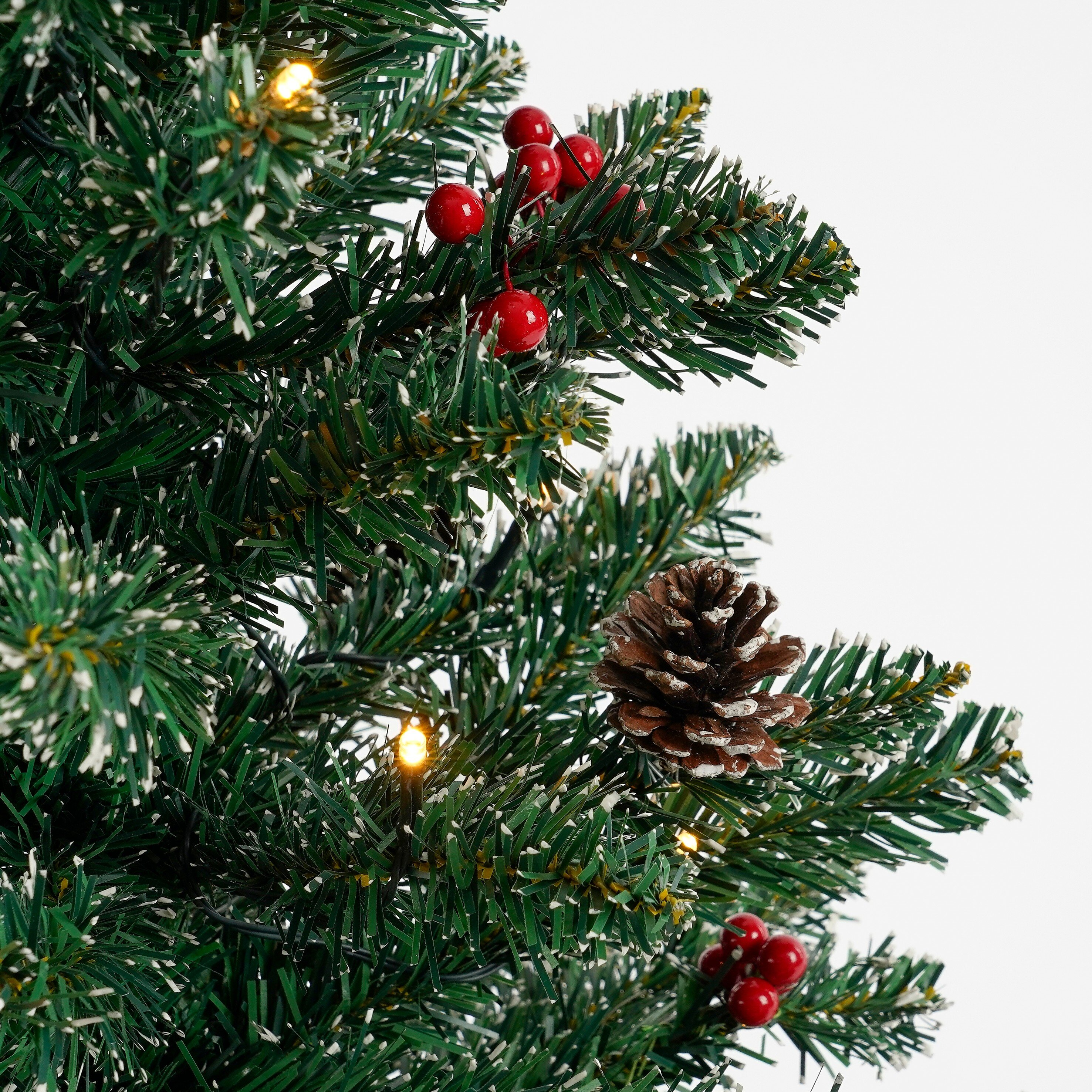 Gros plan sur un sapin de Noël avec des baies rouges, une pomme de pin et des lumières sur fond blanc.