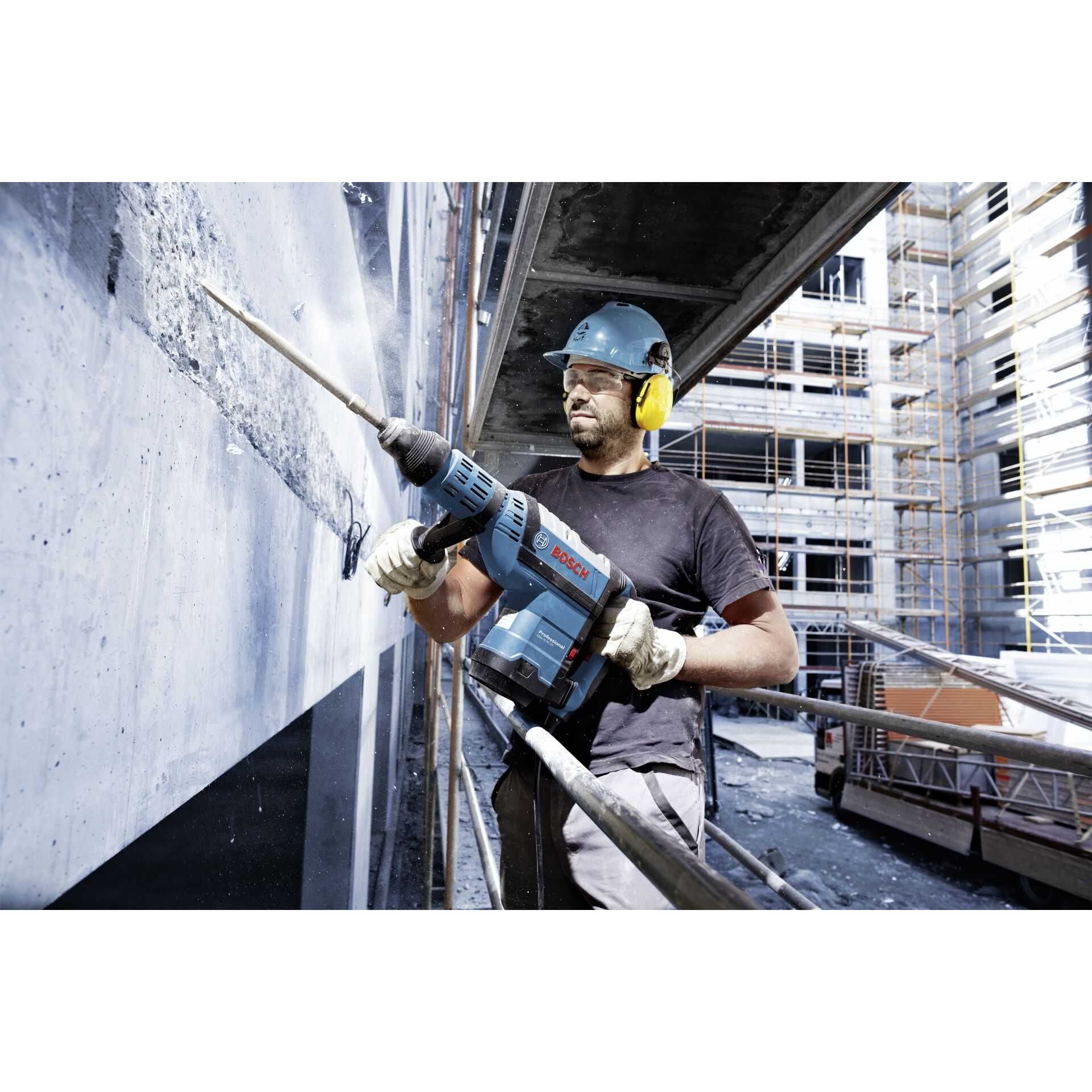 Ein Bauarbeiter verwendet einen Bosch-Bohrhammer an einer Betonmauer. Er trägt Helm, Gehörschutz und Schutzbrille.