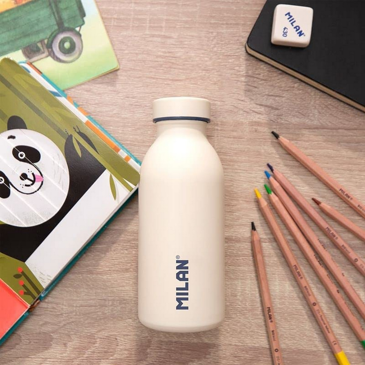 Eine weiße Flasche, Bleistifte, ein Radiergummi und Bücher liegen auf einem Holztisch. Eine Panda-Illustration ist auf einem Buch.