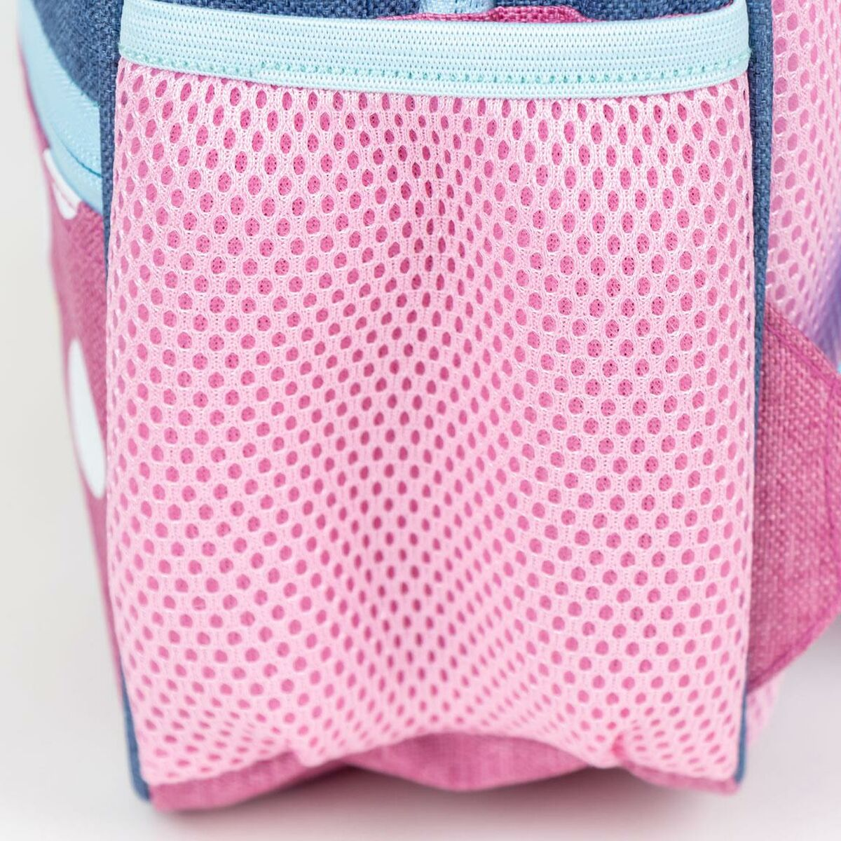 Nahaufnahme einer rosa Netztasche an einem Rucksack. Blauer und rosa Stoff sind sichtbar. Die Tasche ist mit kleinen Löchern gefüllt.