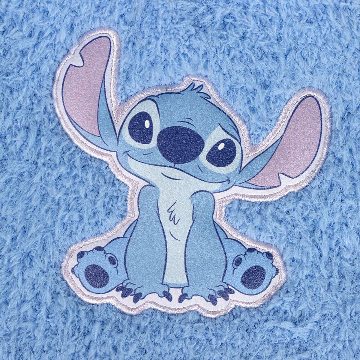 Ein blauer Stitch-Patch auf flauschigem blauem Hintergrund. Stitch lächelt mit großen Ohren und großen Augen. Der Hintergrund ist strukturiert.