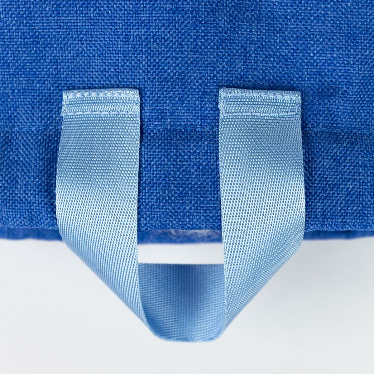 Nahaufnahme eines blauen Stoffes mit zwei hellblauen Trägern, die einen Griff bilden, vor weißem Hintergrund.