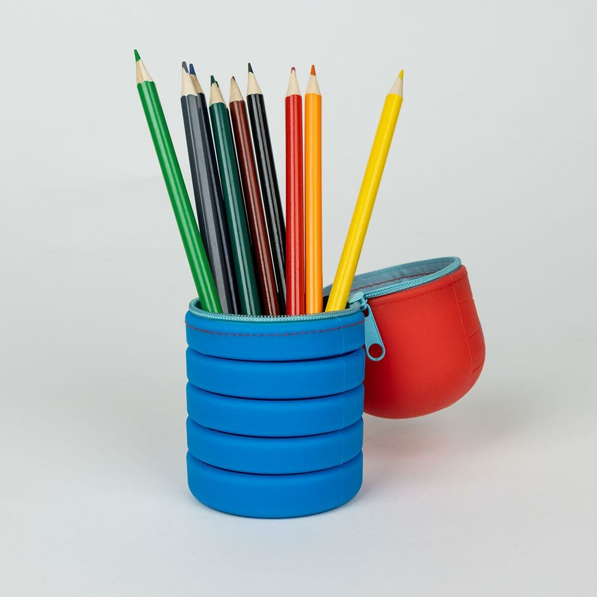 Buntstifte in einem blauen Behälter mit einem roten Federmäppchen. Stifte sind verschiedener Farben. Hintergrund ist weiß.