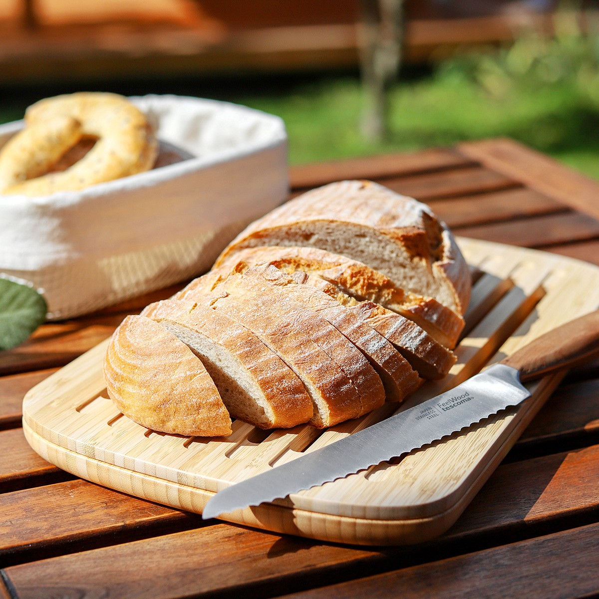 Geschnittenes Brot auf einem Holzbrett mit einem Messer. Ein Korb mit Brot im Hintergrund. Der Tisch ist aus Holz.