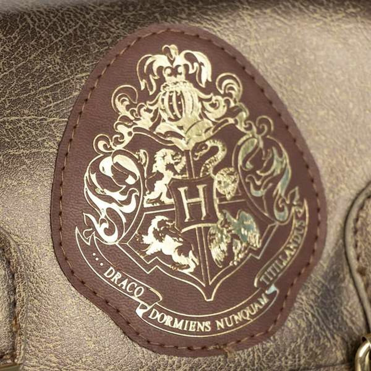 Nahaufnahme eines braunen Lederaufnähers mit dem Hogwarts-Wappen. Goldene Schrift und Bild. Der Aufnäher ist auf einer strukturierten Lederoberfläche genäht.
