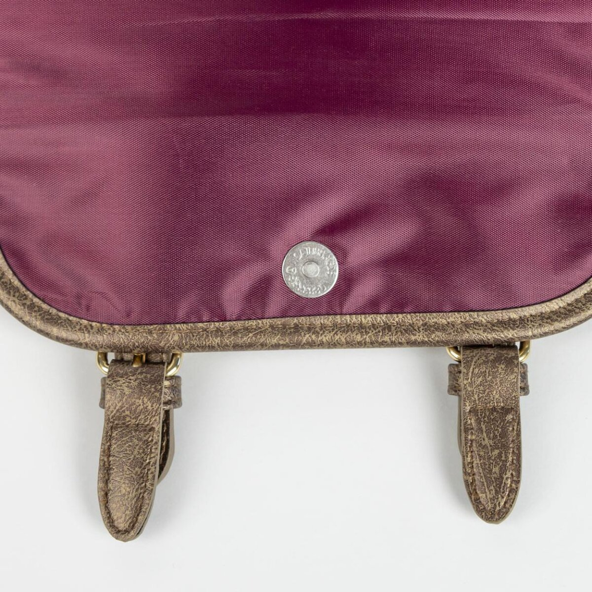 Nahaufnahme einer weinroten Tasche mit Metallverschluss und Lederriemen. Die Tasche befindet sich auf weißem Hintergrund.