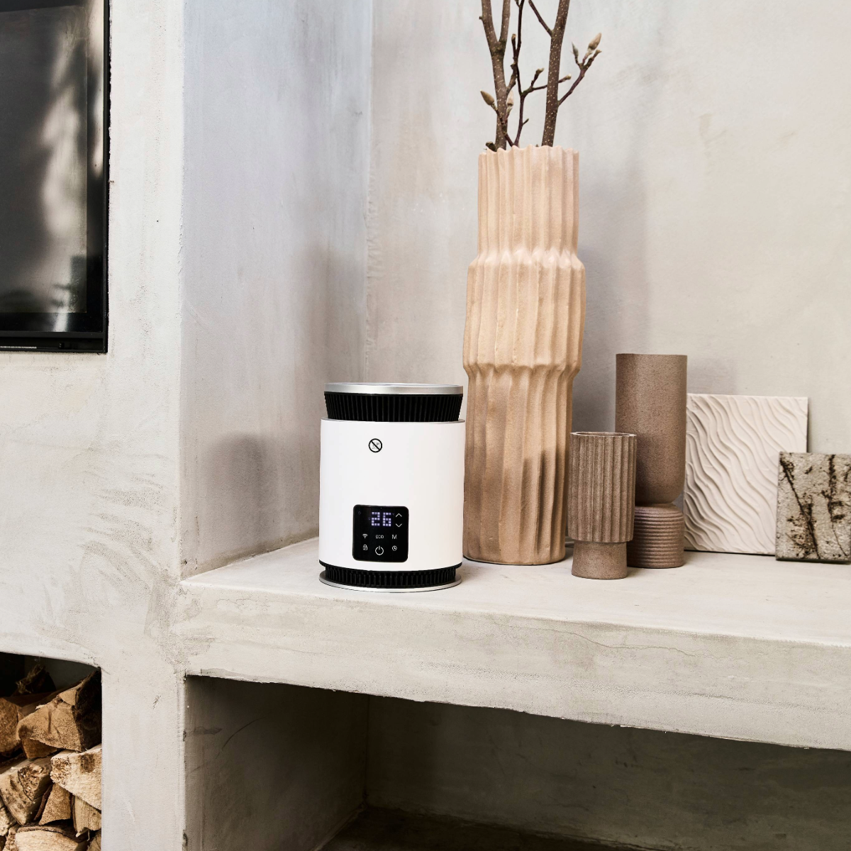Un purificatore d'aria bianco con display digitale, posto su una mensola di cemento, accanto a vasi e un pannello decorativo. Sotto è visibile legna da ardere.