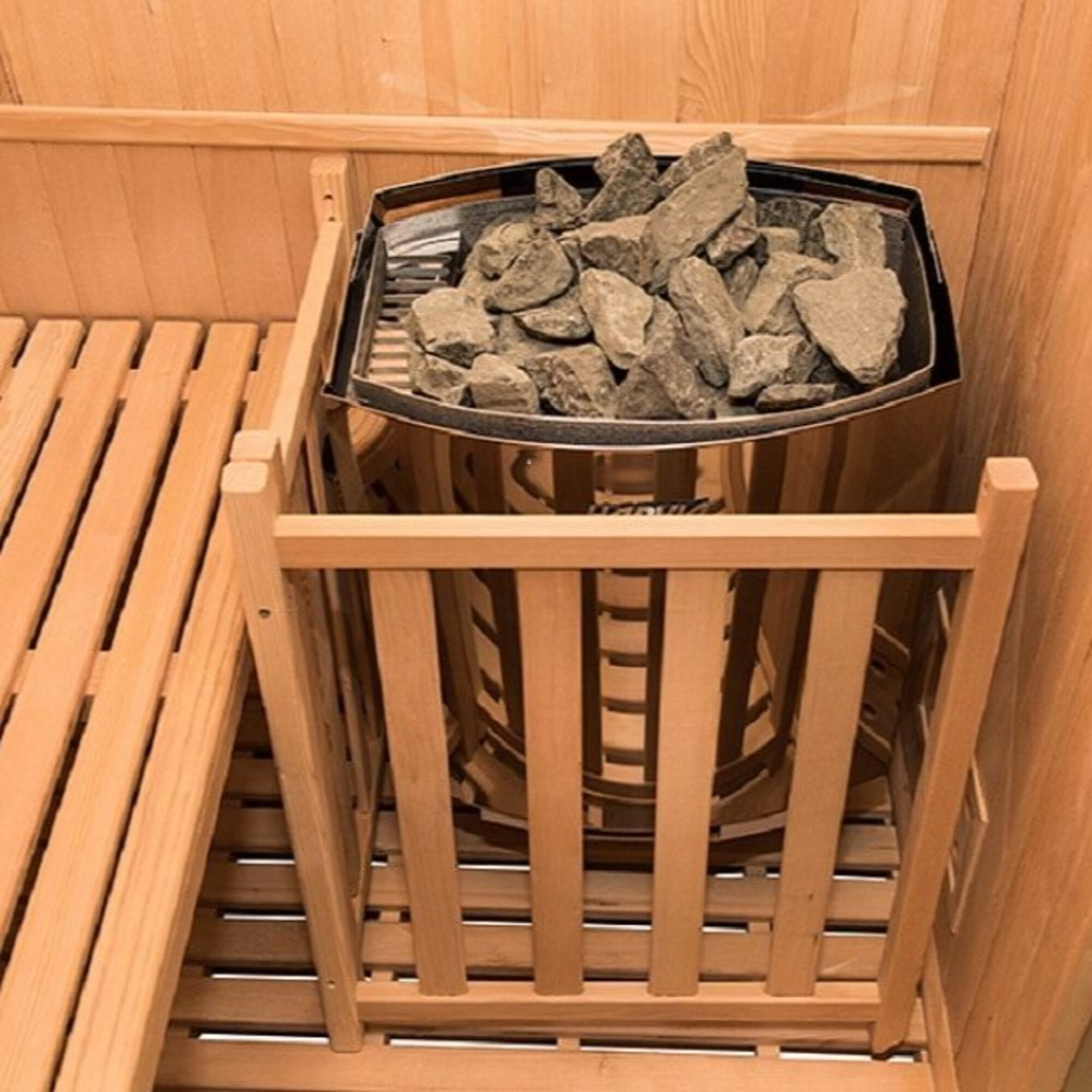 Interior de sauna con un calentador lleno de rocas. Bancos y paredes de madera. El calentador está en un recinto de madera.