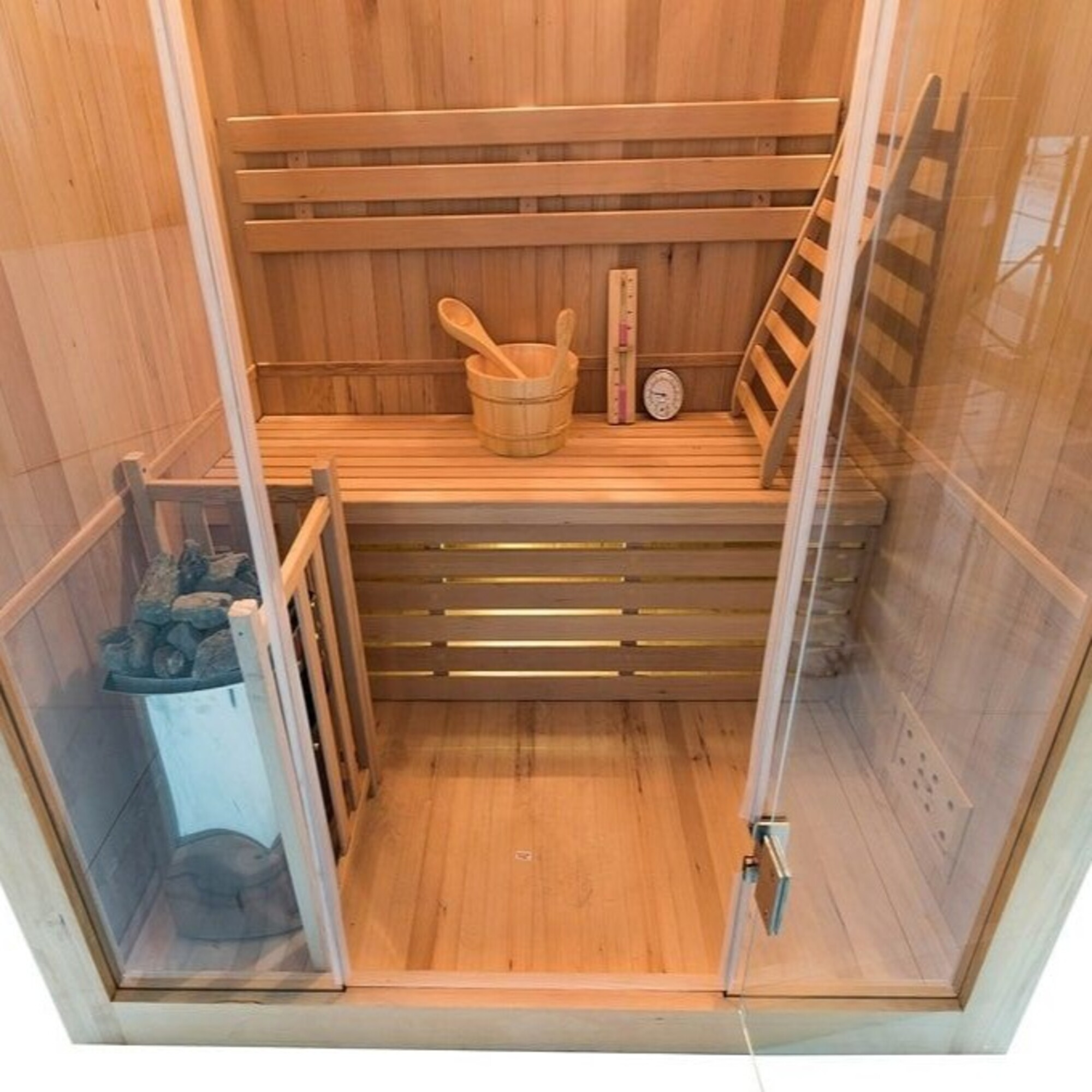 Interior de sauna de madera con banco, cubo, termómetro y escalera. Puertas y paredes de vidrio.
