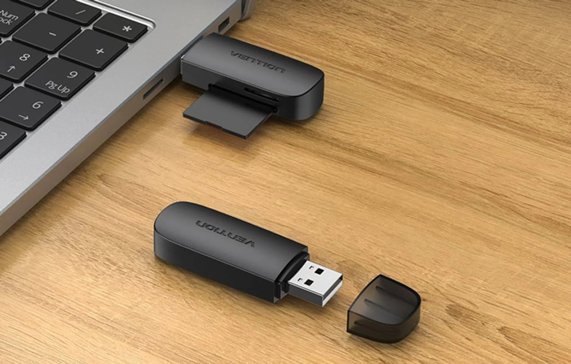 Czarny pendrive i czytnik kart na drewnianej powierzchni obok laptopa. Pendrive ma zdjętą nasadkę.