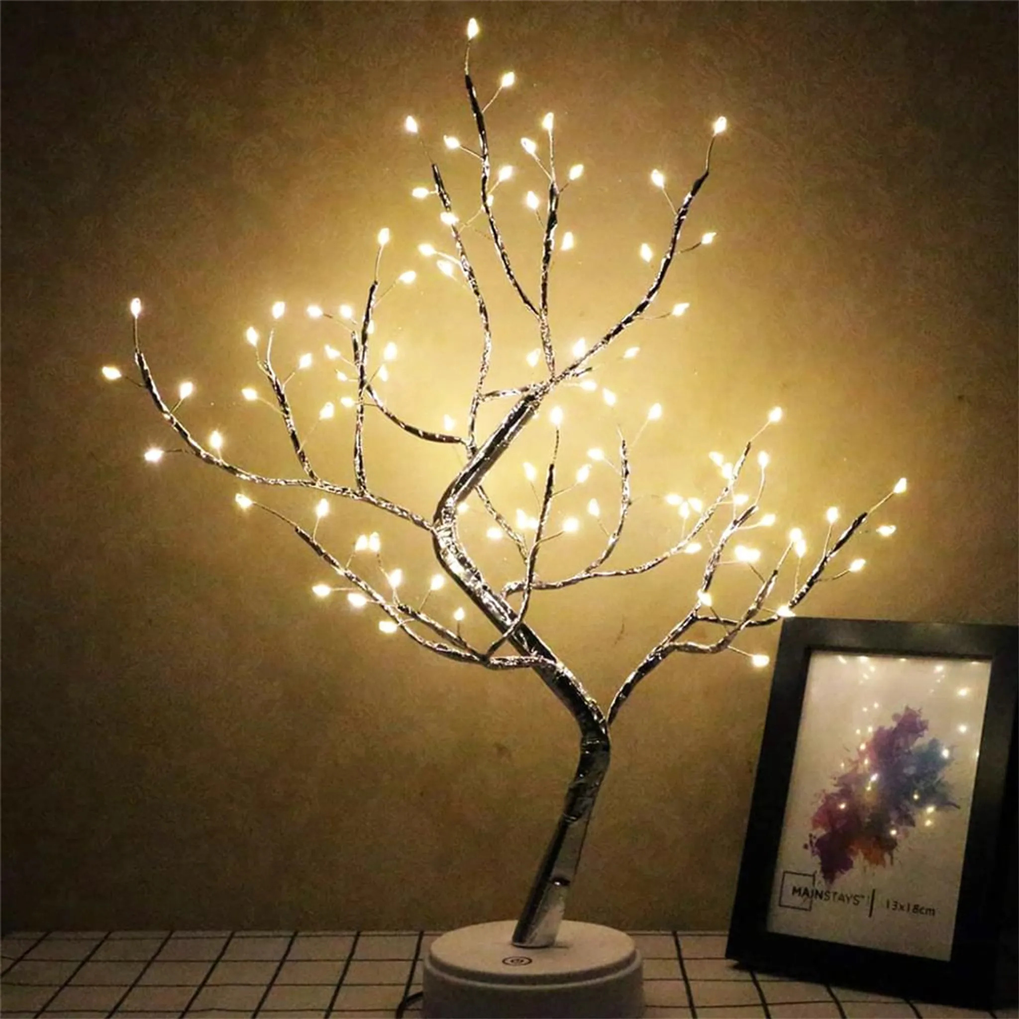 Dekorative LED-Baumlampe mit leuchtenden Lichtern. Daneben steht ein gerahmtes Bild auf kariertem Untergrund.
