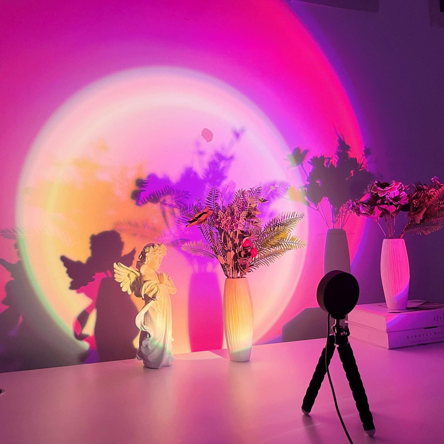 Ein Raum, der von einer Sonnenuntergangslampe beleuchtet wird. Eine Engelsstatue, Vasen mit Blumen und ein kleines Stativ sind sichtbar. Der Hintergrund ist farbig.