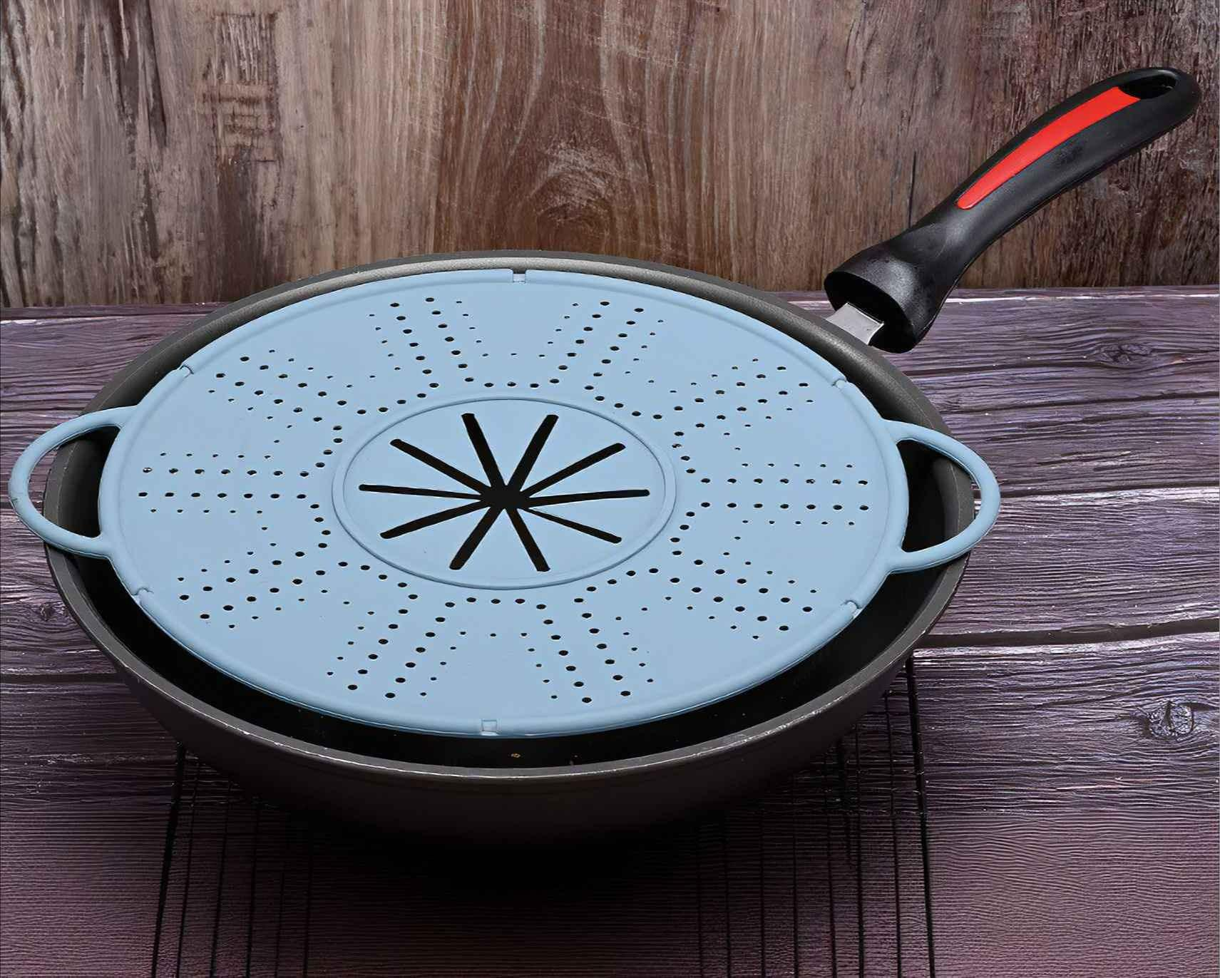 Ein blauer Siebdeckel liegt in einer Pfanne mit schwarzem Griff. Der Hintergrund ist eine Holzoberfläche.