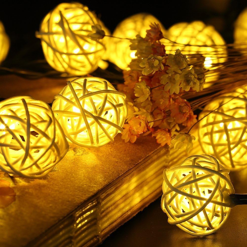 Beleuchtete Rattan-Kugellichter auf einem Buch mit Blumen. Warme gelbe Lichter und Weichzeichnung schaffen eine gemütliche Atmosphäre.