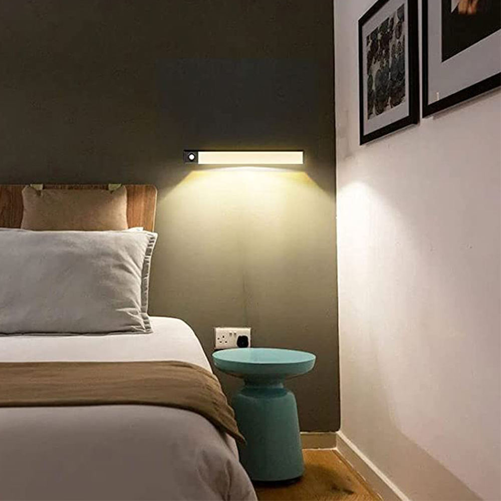 Schlafzimmerszene mit Bett, kleinem blauen Tisch und Wandleuchte, die die Wand beleuchtet. Kunstwerke sind sichtbar.