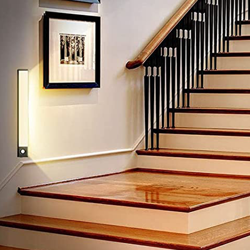 Holztreppe mit schwarzen Geländern und einem Holzhandlauf. An der Wand hängt ein Bild, und eine Leuchte ist vorhanden.