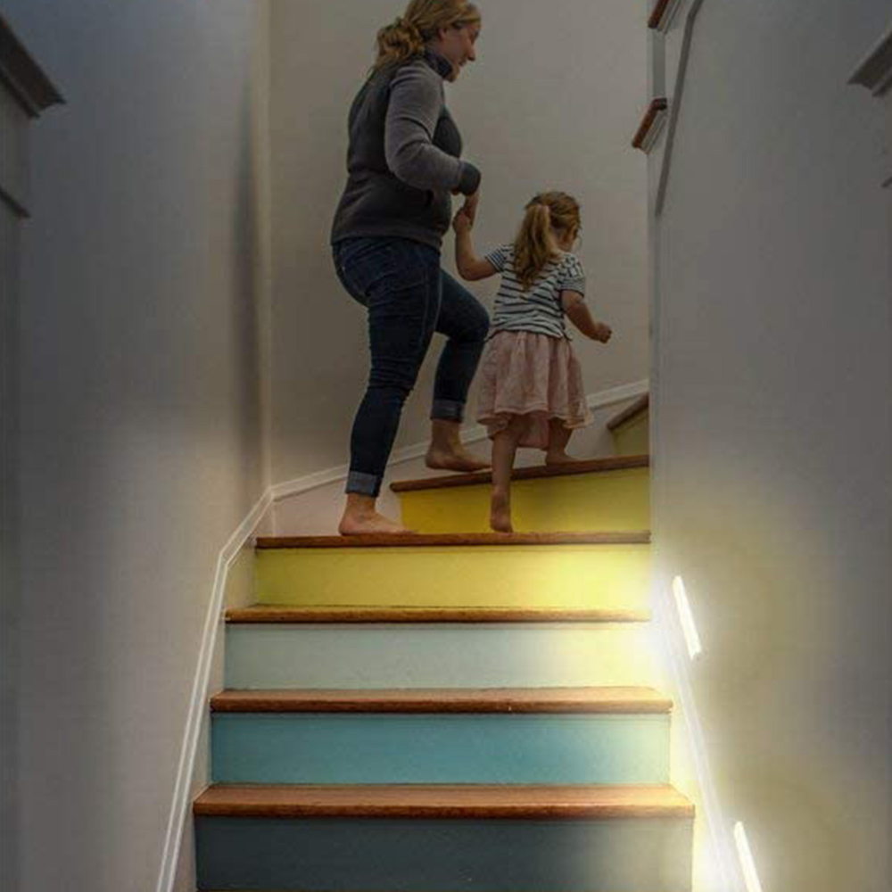 Eine Frau und ein Kind steigen die bunten Treppen hinauf und halten sich an den Händen. Die Treppen haben gelbe, blaue und graue Stufen.