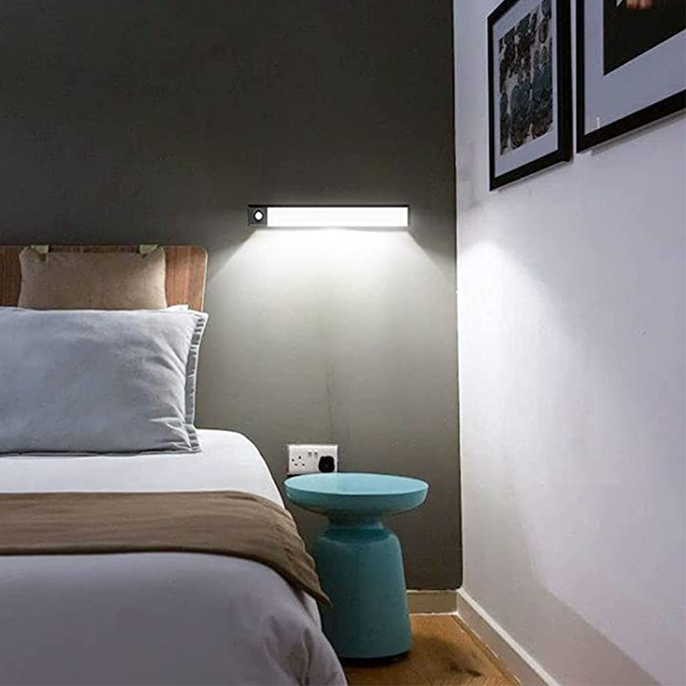 Schlafzimmer mit Bett, Beistelltisch und Wandleuchte. Bilder an der Wand. Der Raum ist schwach beleuchtet.