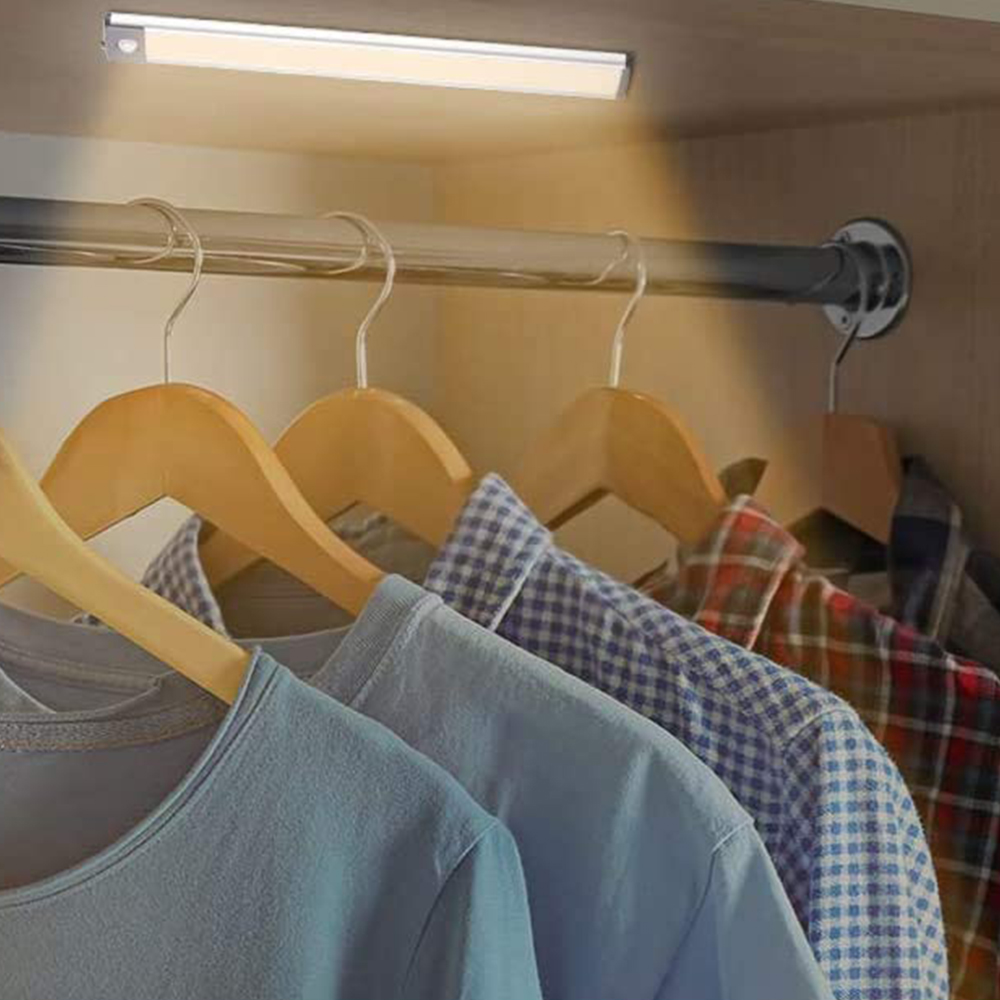 In einem Schrank beleuchtet ein Licht hängende Kleidung. Hemden an Kleiderbügeln sind unter einer Leuchte sichtbar.