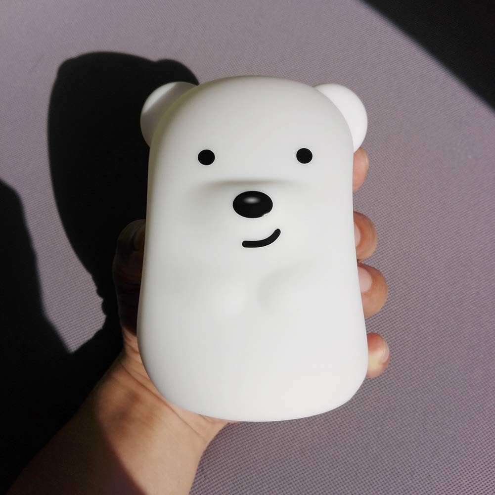 Eine weiße bärenförmige Lampe wird in einer Hand gehalten. Sie hat schwarze Augen, Nase und einen lächelnden Mund. Ein Schatten ist im Hintergrund.