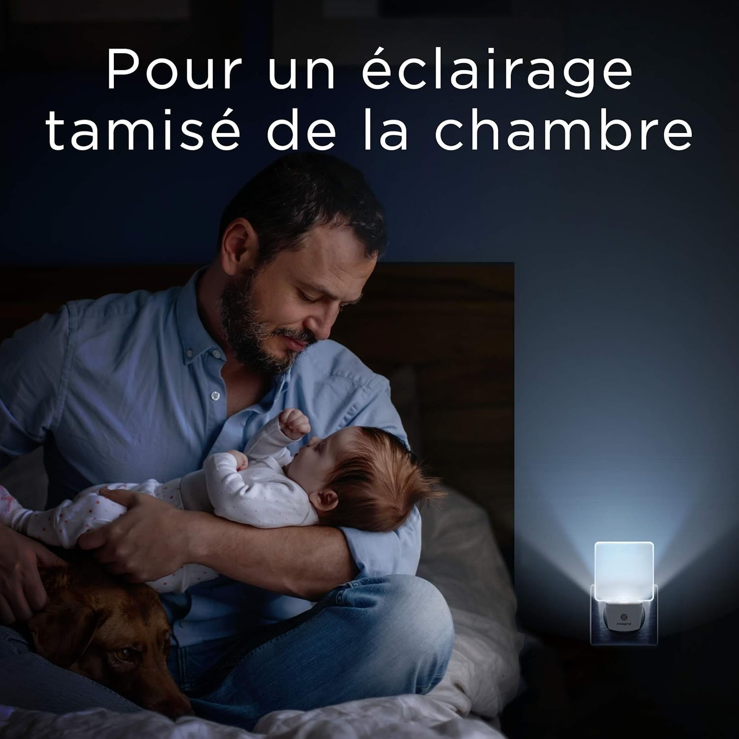 Ein Mann hält ein Baby, ein Hund ruht in der Nähe. Text: 'Für eine gedämpfte Schlafzimmerbeleuchtung'. Ein Nachtlicht ist eingesteckt.