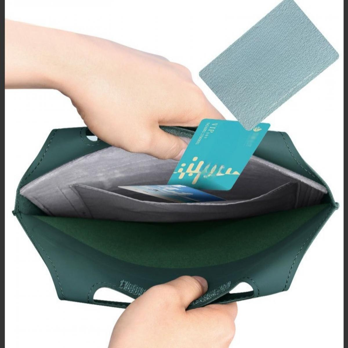 Eine Hand steckt eine Karte in eine grüne Ledertasche. Eine weitere Karte und eine Lederabdeckung sind ebenfalls sichtbar.